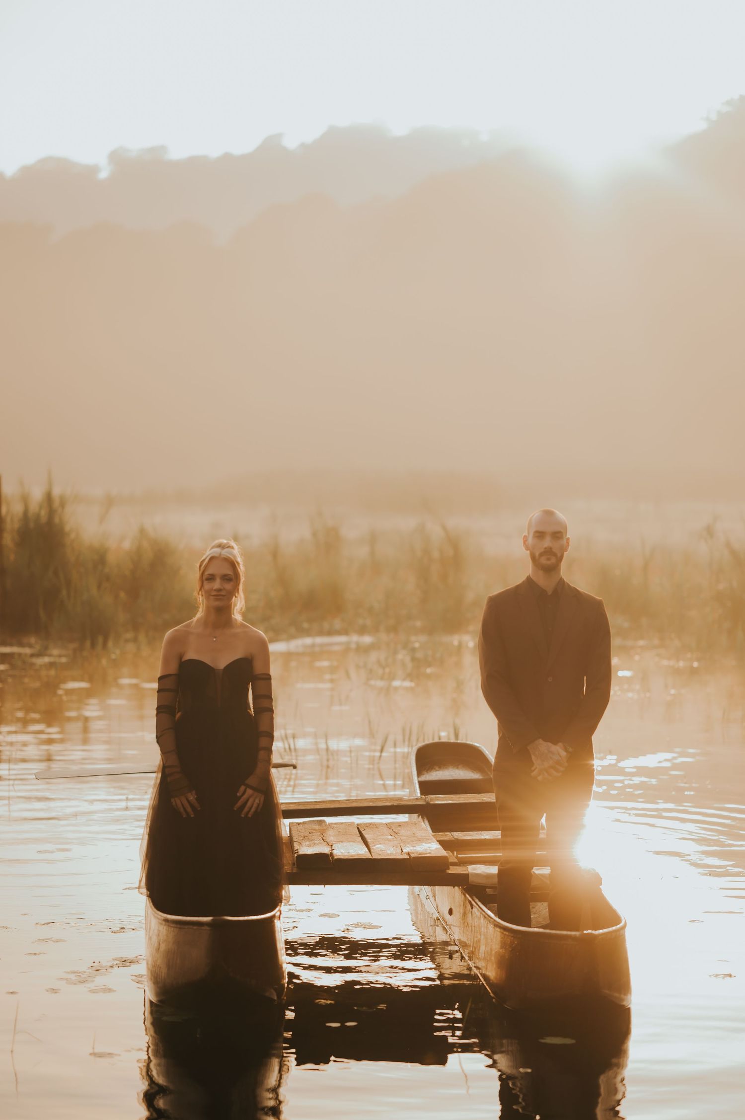 Two people in canoes on a tranquil lake during golden hour with sunlight filtering through the mist.