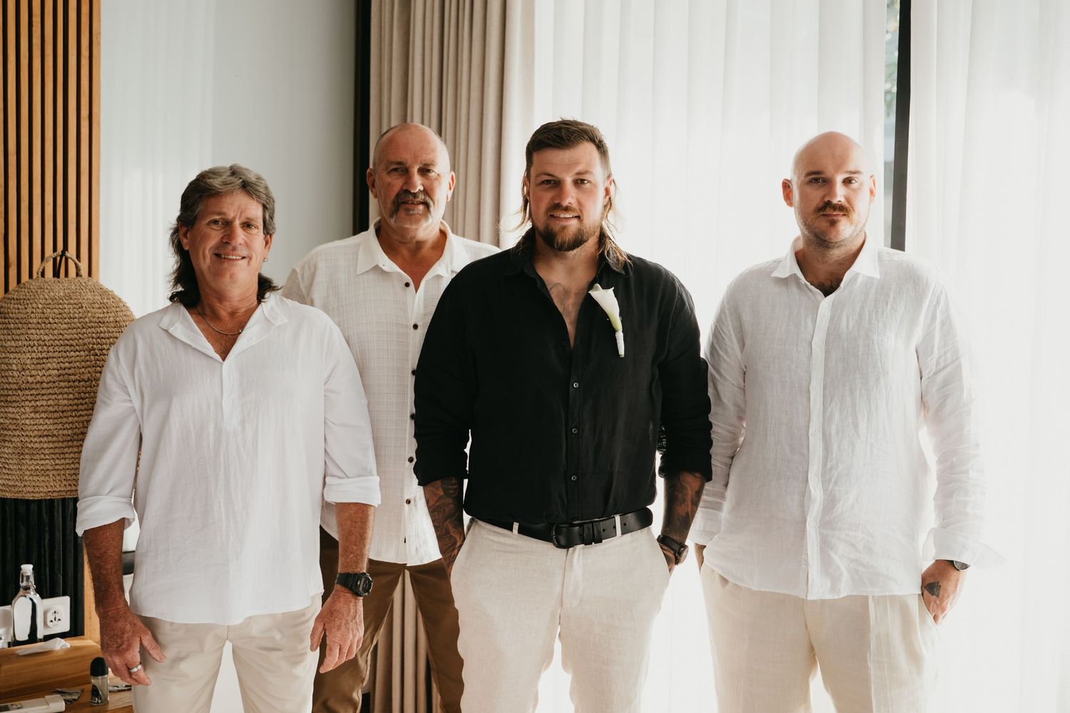 Four men in white and black shirts smile together indoors in a bright modern setting.