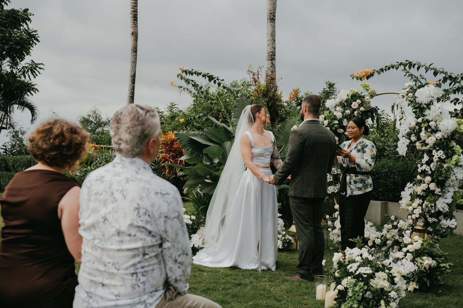 Bride and groom exchanging vows at floral arch during intimate outdoor garden wedding.