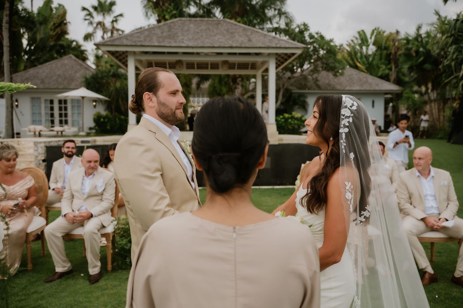 Bride and groom exchange vows outdoors at an elegant garden wedding ceremony with seated guests.