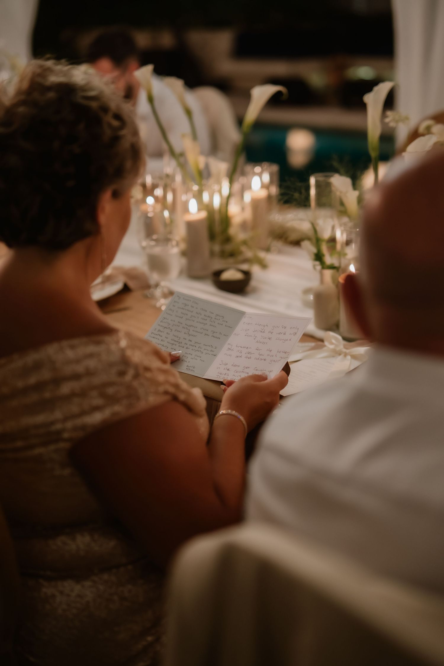 Guest reading handwritten letter at candlelit wedding reception table with white calla lilies.