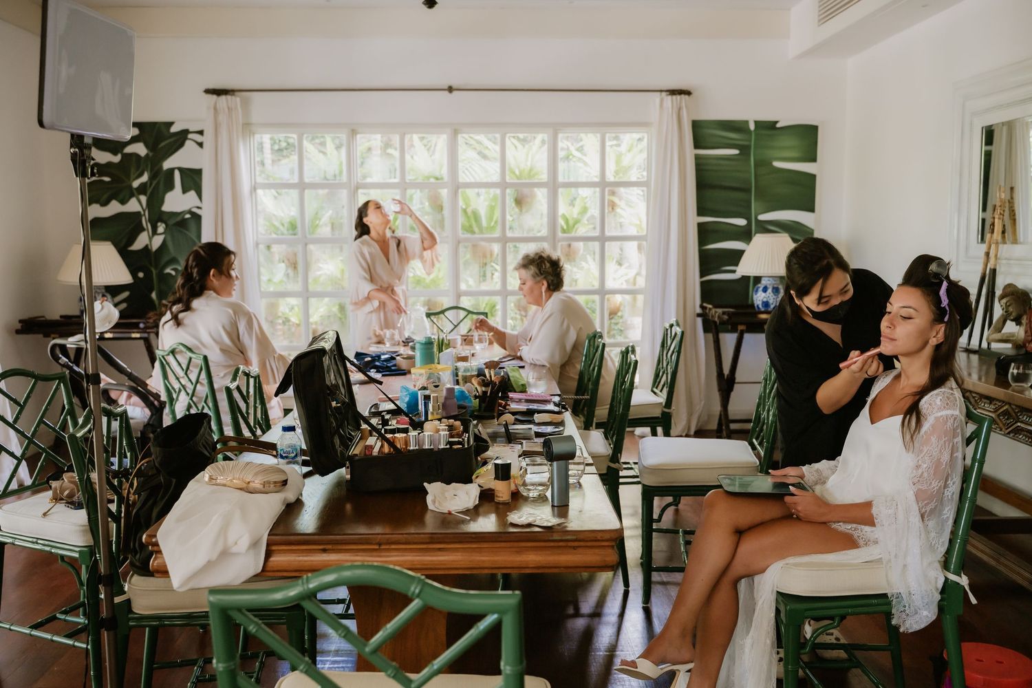 Bridesmaids getting hair and makeup done in a bright tropical villa room before a wedding ceremony.