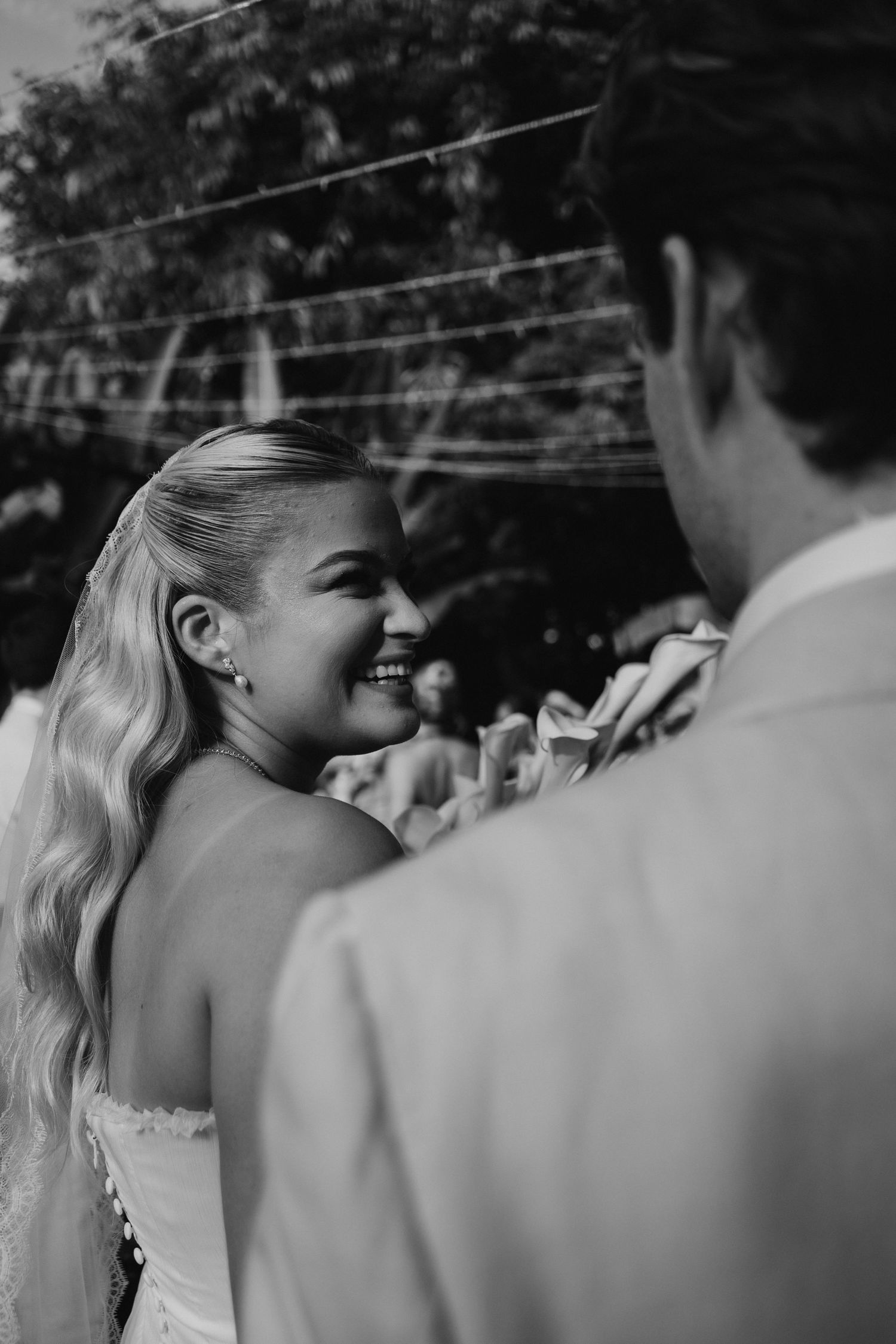 Black and white photo of radiant bride smiling at groom during outdoor wedding ceremony.