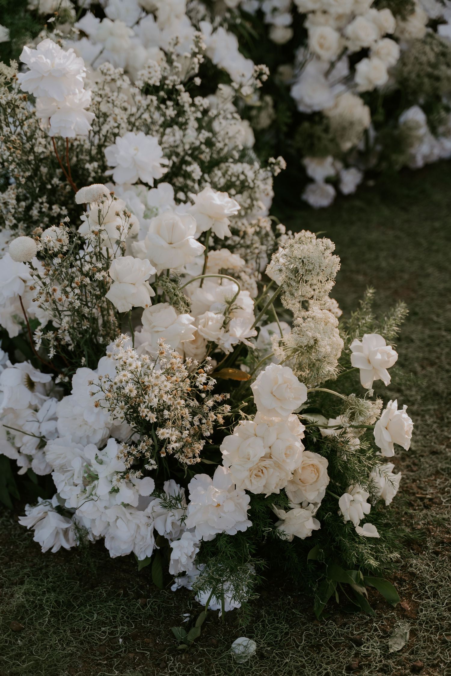 Lush arrangement of white roses, peonies, and baby's breath flowers for an outdoor wedding ceremony.