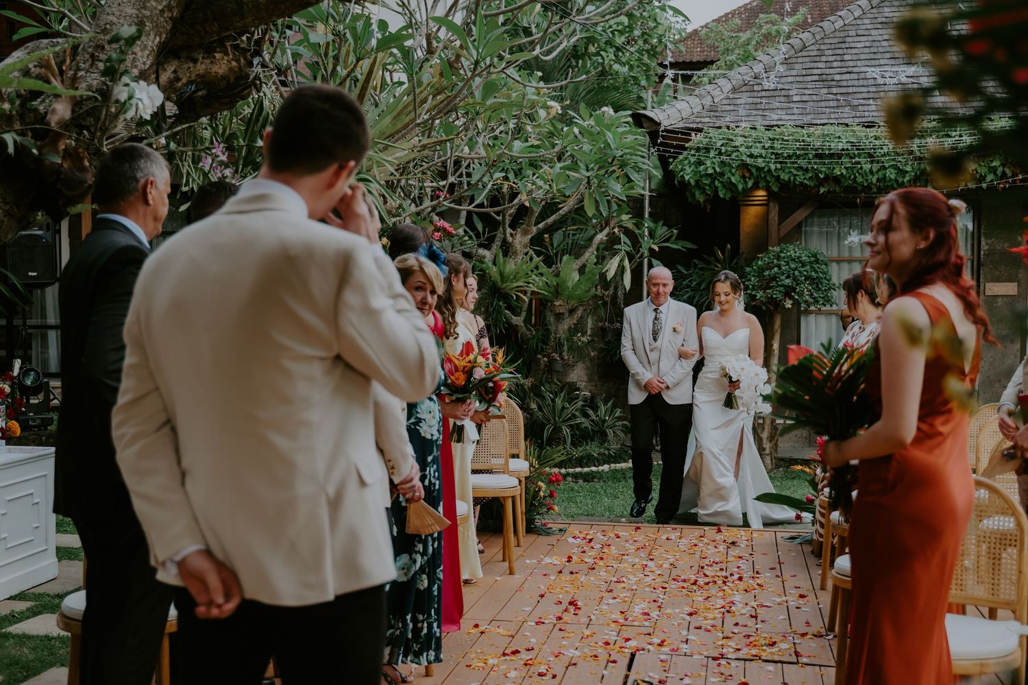 Guests watching as a bride walks down a flower-petal aisle at an elegant outdoor garden wedding.