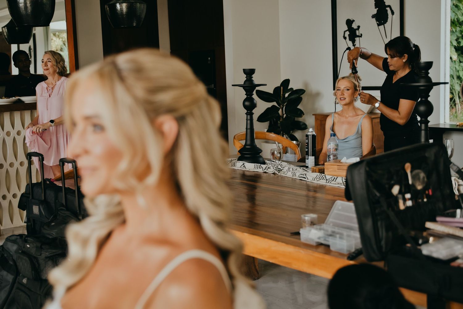 Bride getting ready with bridesmaids and makeup artists in a bright wedding preparation room.