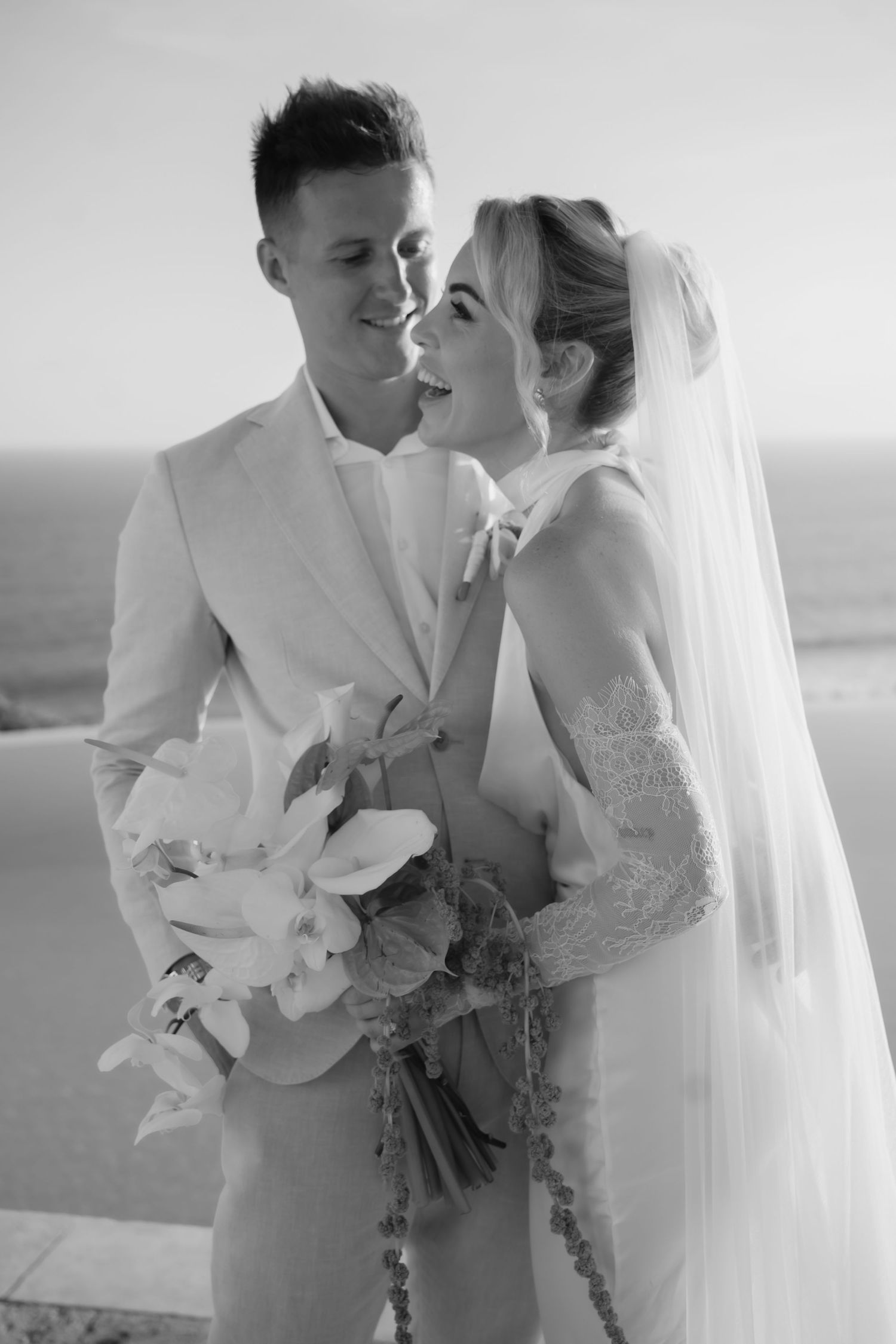 Black and white portrait of wedding couple sharing intimate moment by the sea.