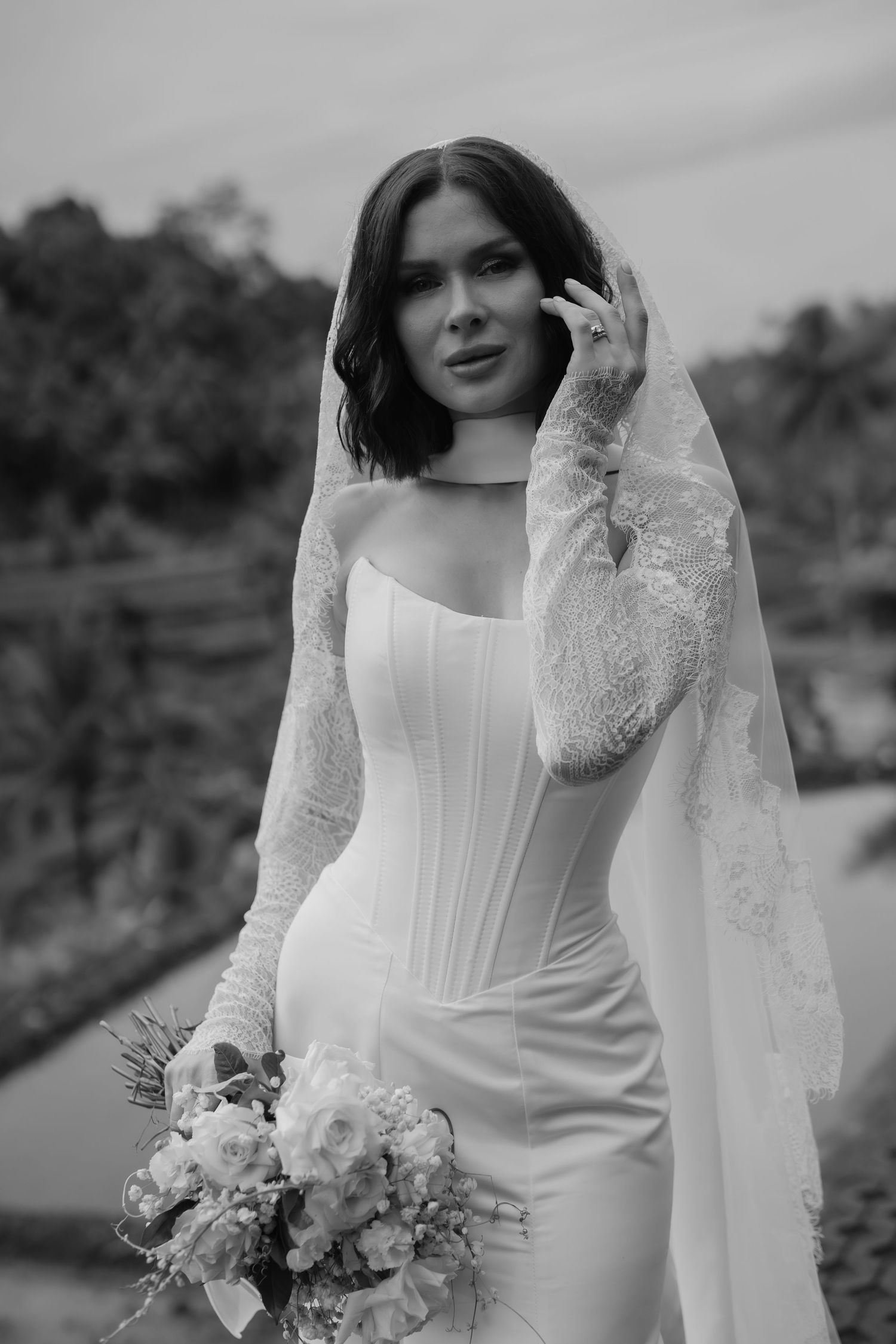 A bride in a sleek white corset wedding dress holds a pastel bouquet in black and white photography.