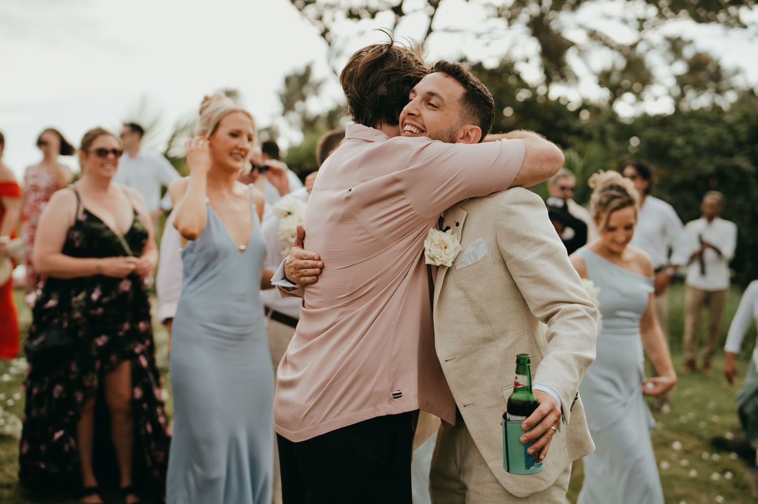 Two men share a warm embrace at an outdoor wedding reception celebration.