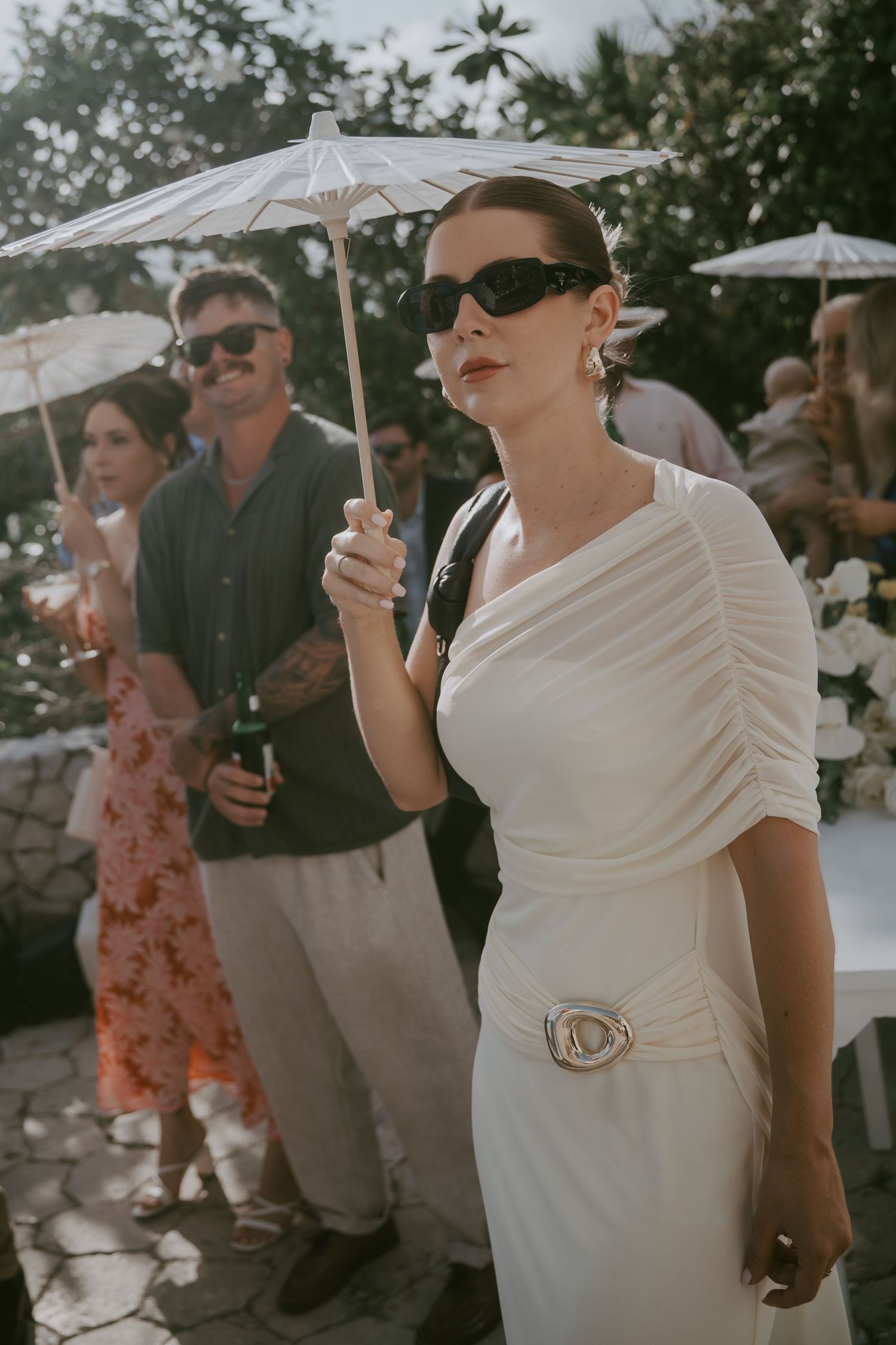 Wedding guests enjoying drinks under parasols at an outdoor celebration.