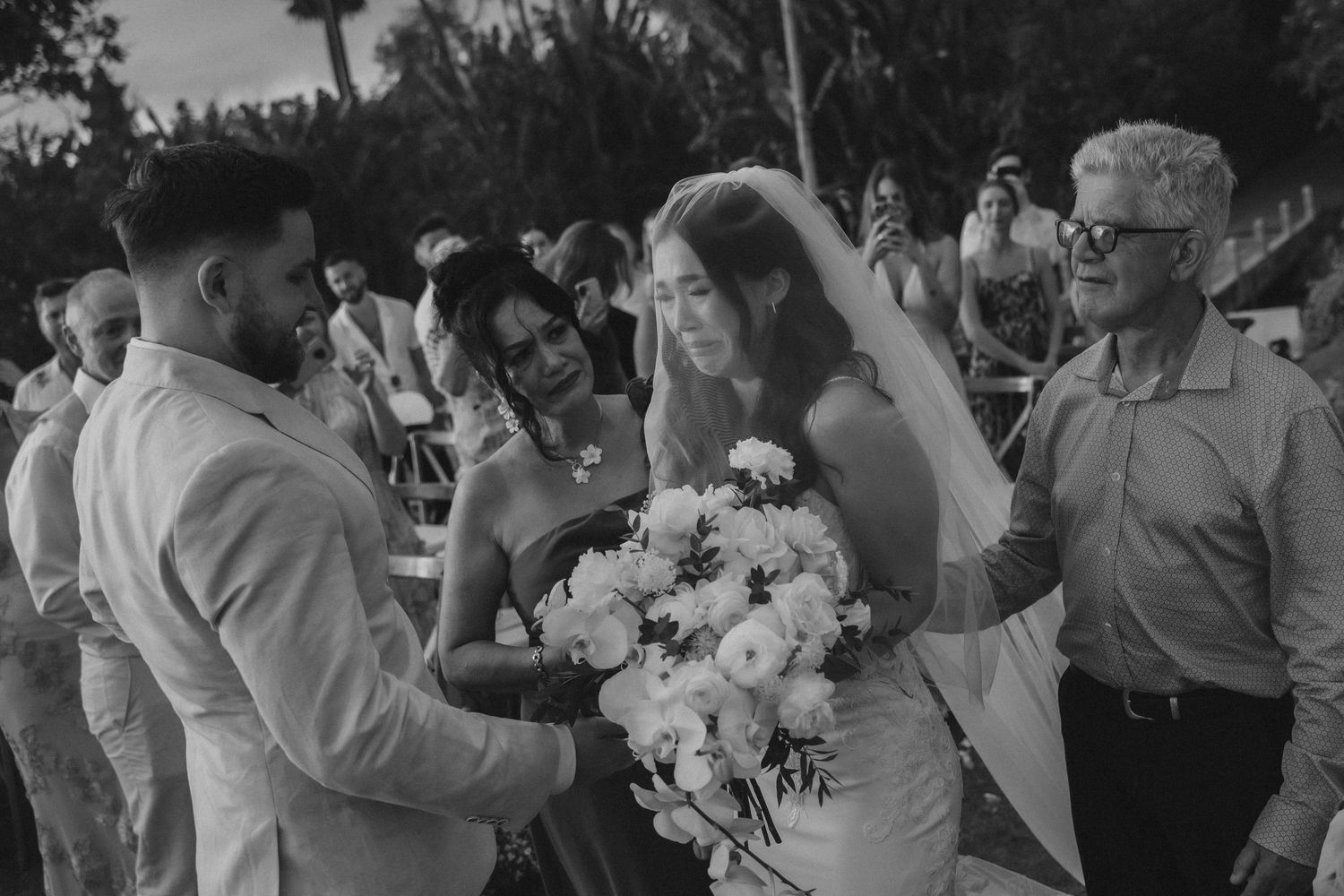 Wedding guests dance and celebrate together during an outdoor reception with palm trees in the background.
