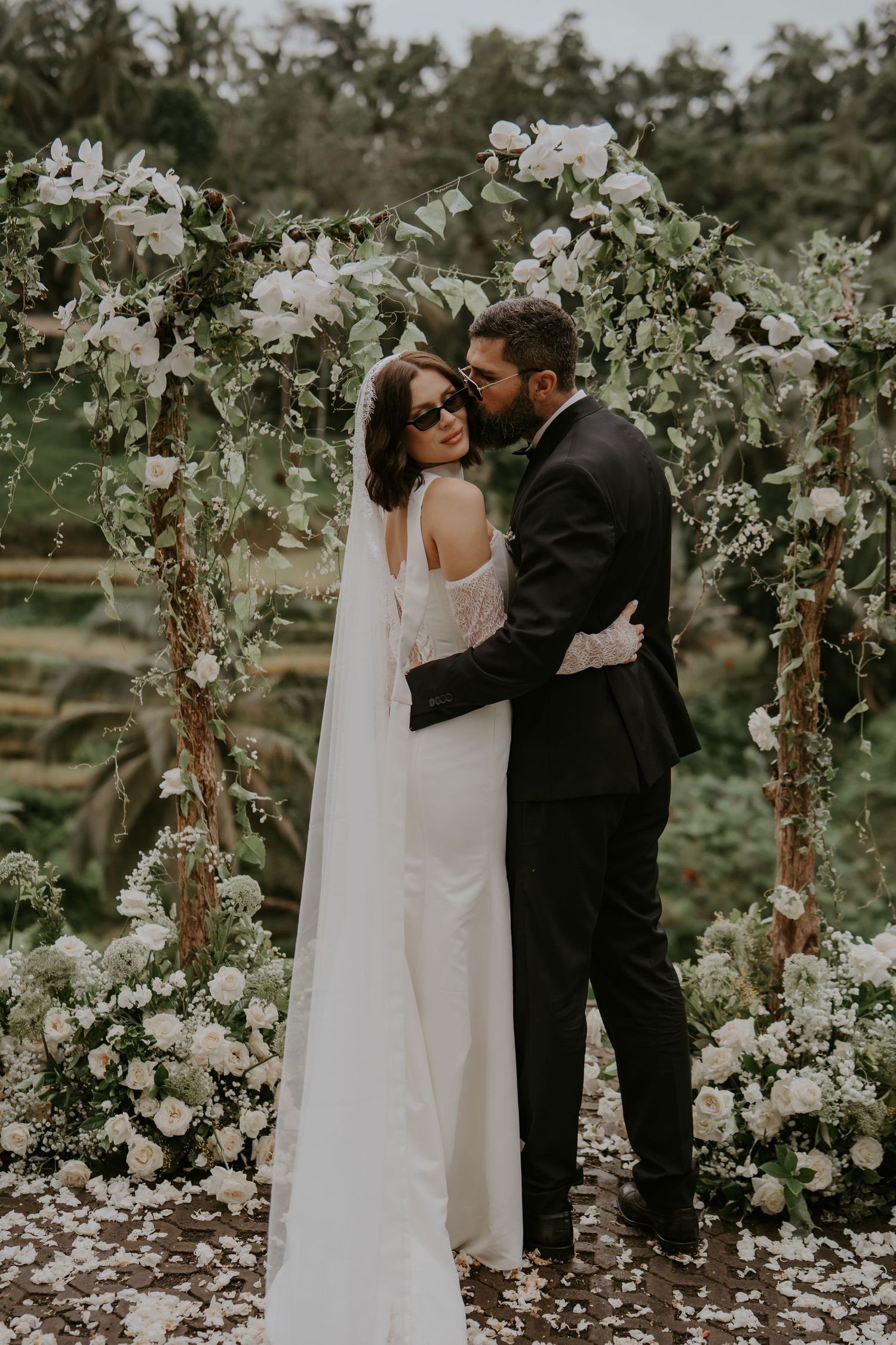 Romantic wedding couple shares intimate moments under floral archway in garden setting.