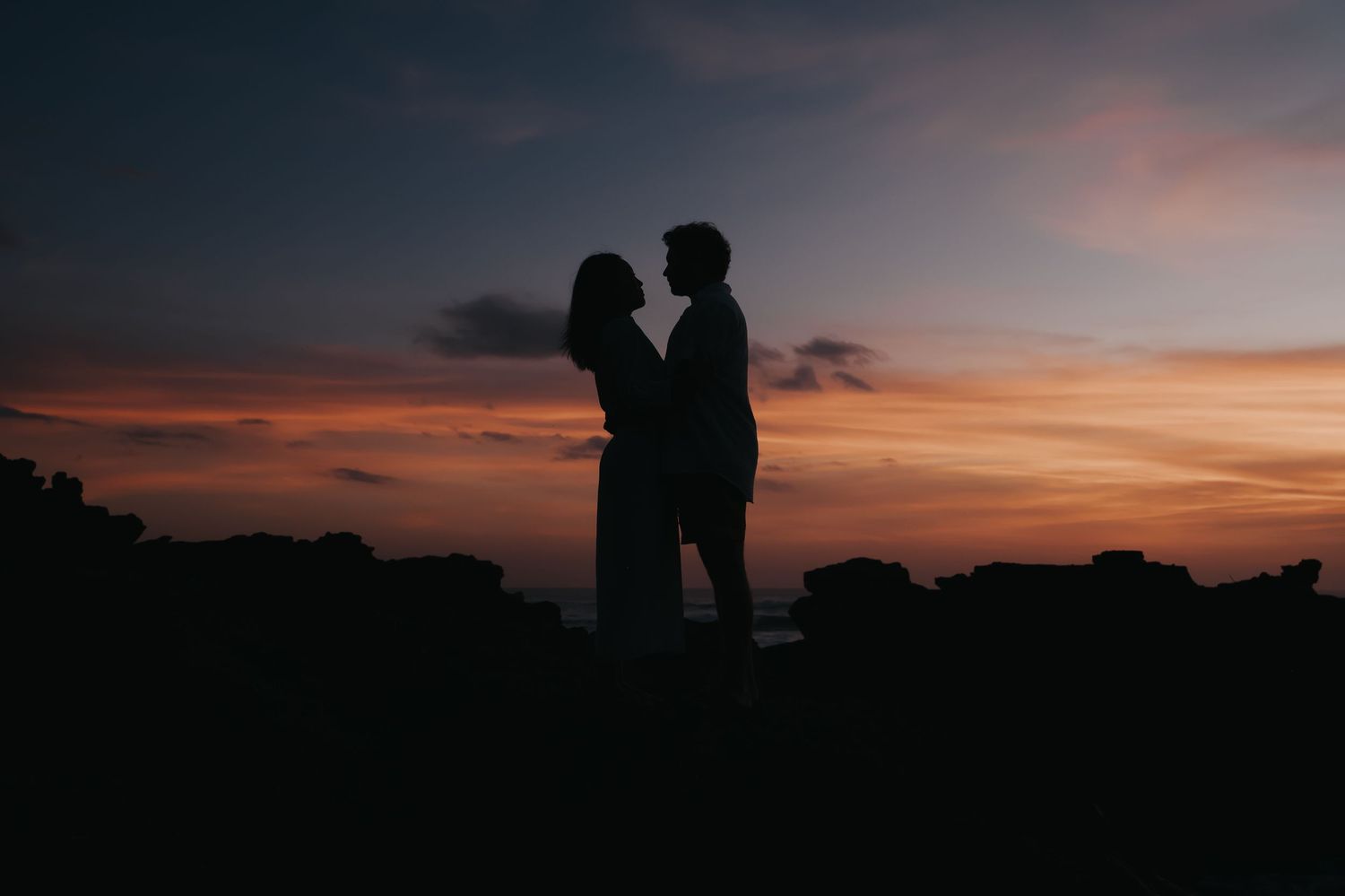 Silhouettes of people standing together against a dramatic orange and purple sunset sky over a dark landscape.