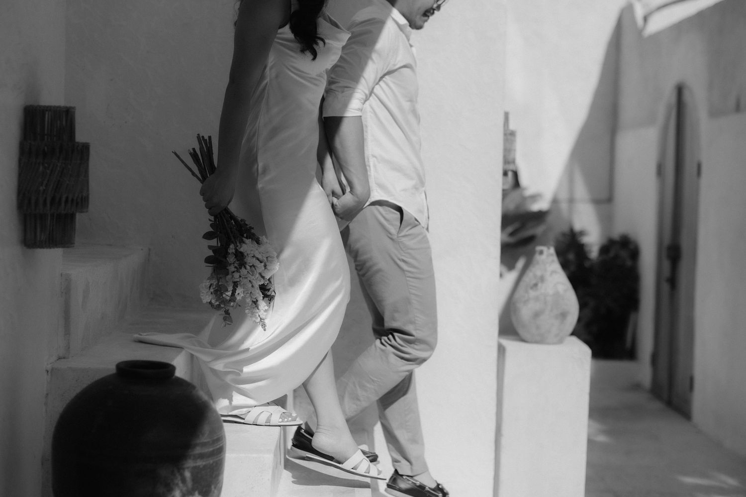 Black and white photo of a couple in wedding attire descending outdoor steps at a Mediterranean venue.