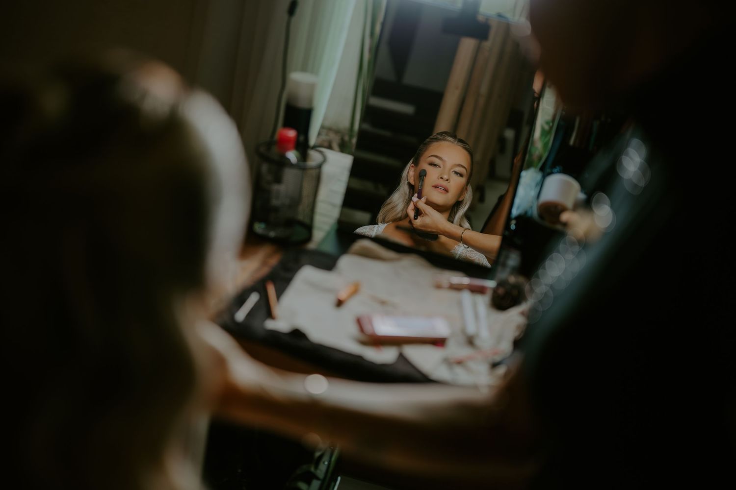 Bride getting makeup applied while reflected in a mirror during wedding preparation.