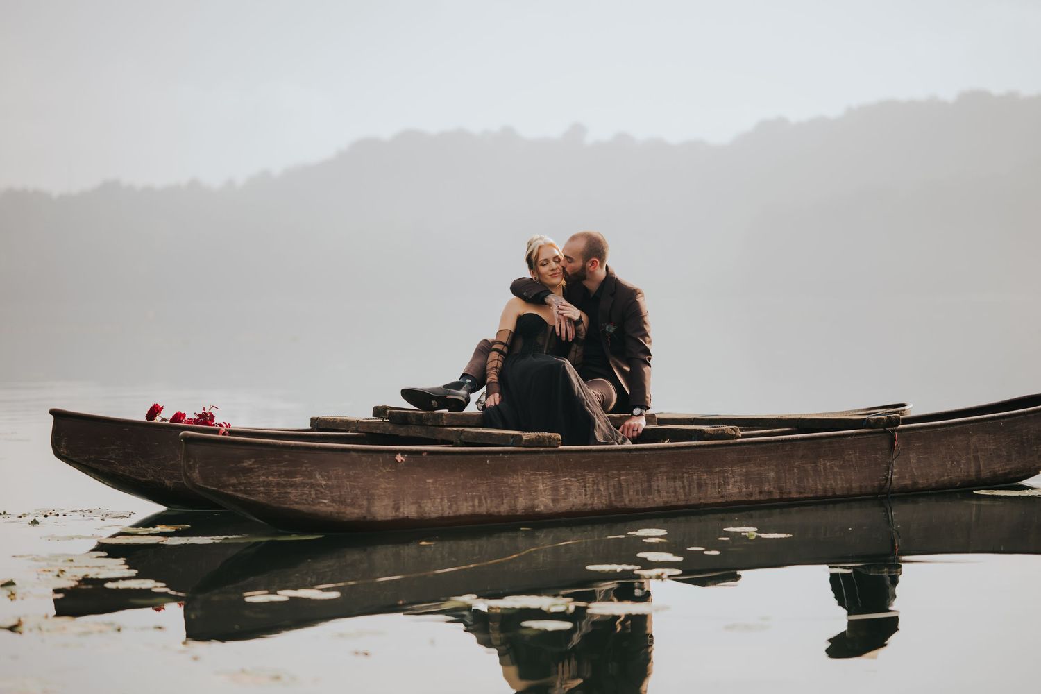 A romantic couple embraces while sitting in a wooden canoe on a foggy lake.