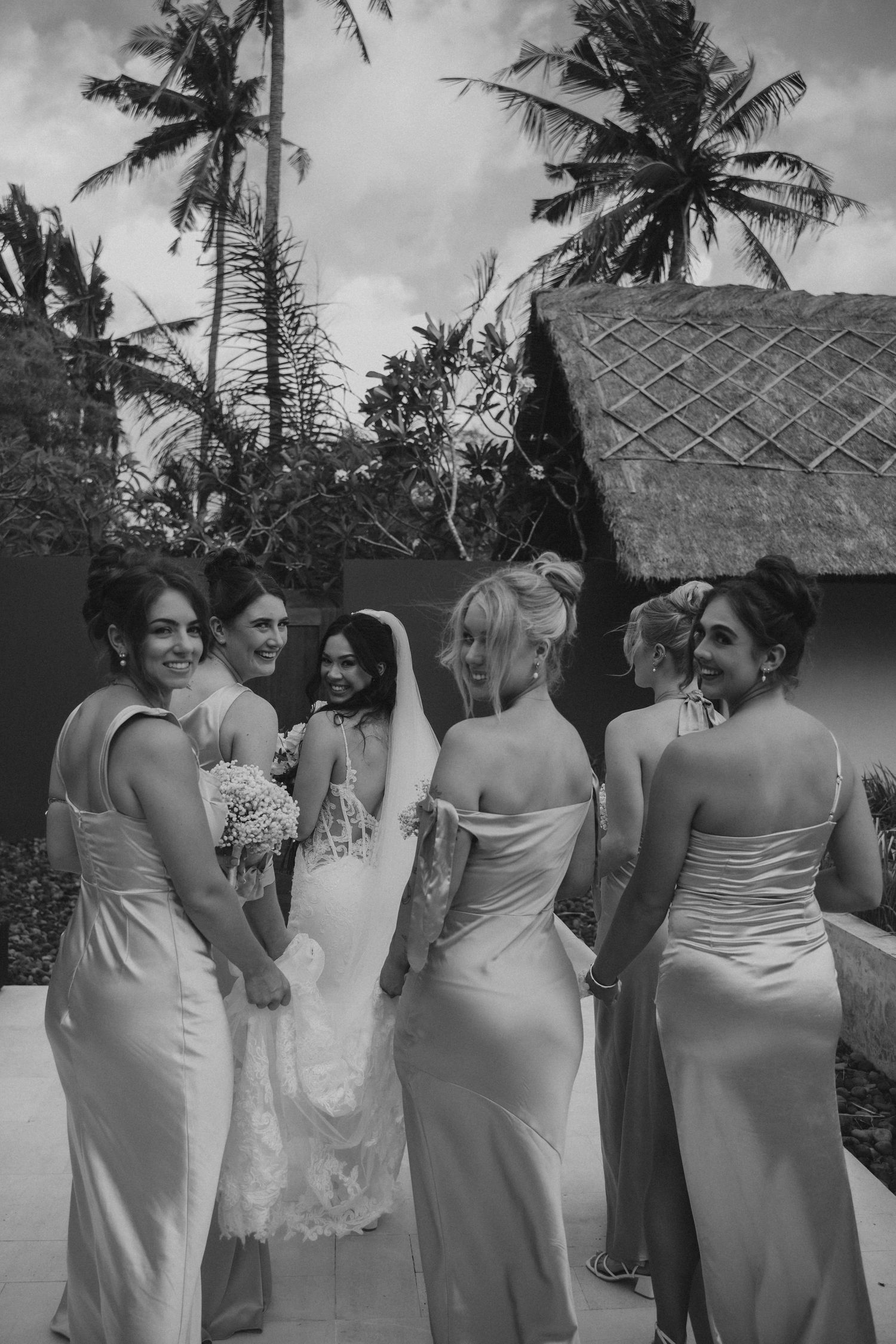 A sequence of black and white photos showing bridesmaids in matching light-colored dresses at a tropical beach wedding.