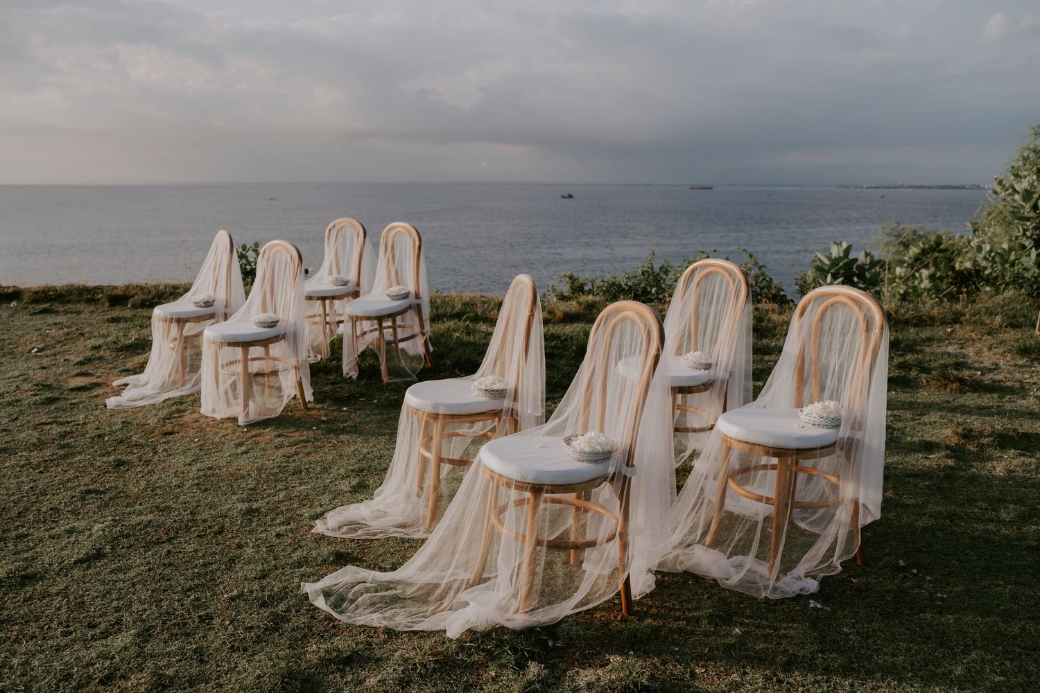 Elegant draped chairs arranged on a clifftop lawn overlooking the ocean at a romantic outdoor wedding ceremony.