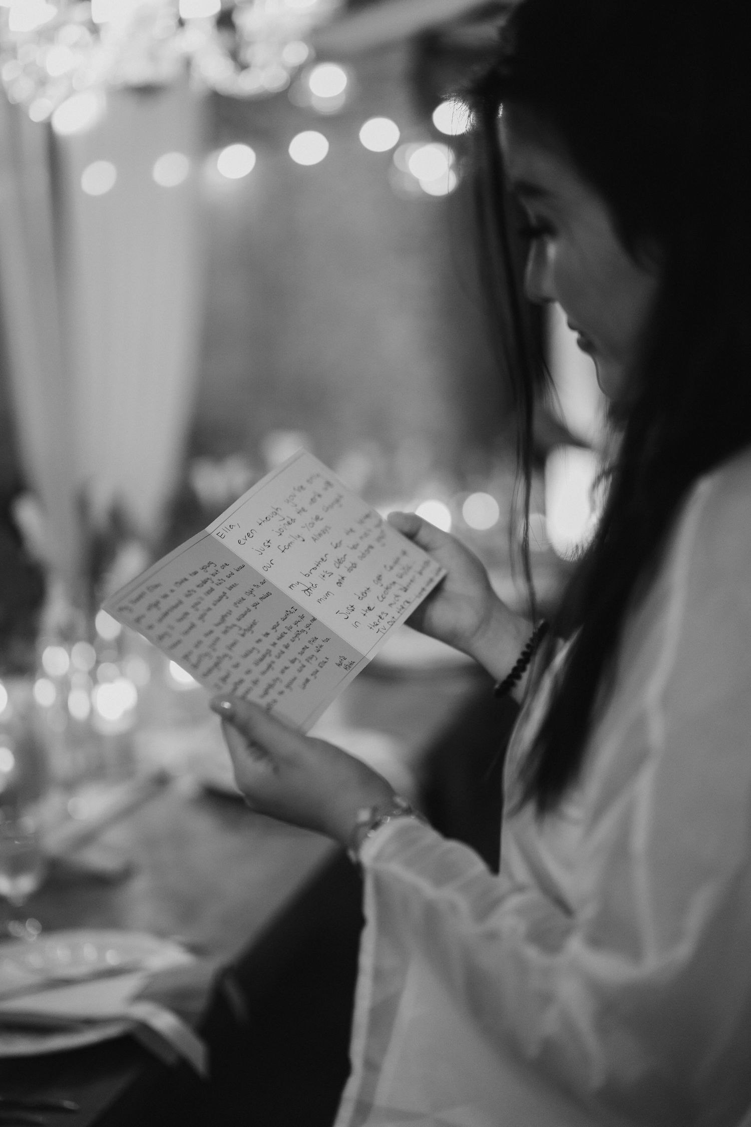 Black and white photo of a woman reading handwritten vows at a candlelit wedding reception table.