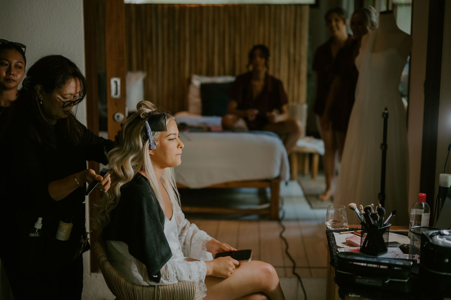 Bride getting hair styled by hairstylist in hotel room before wedding ceremony.