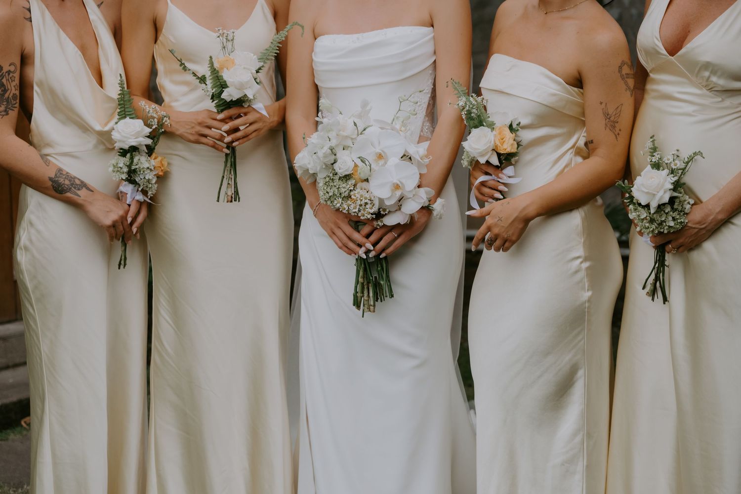 Close-up of bride and bridesmaids in ivory satin gowns holding elegant white and green bouquets.