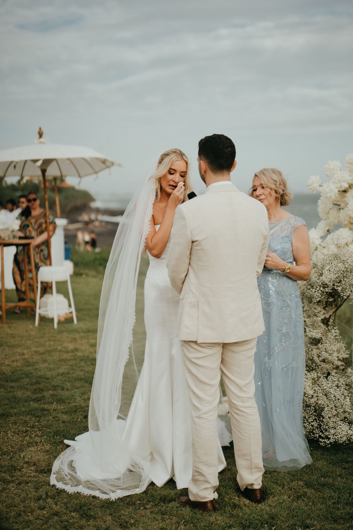 Bride in white gown and veil exchanges vows with groom at oceanside wedding ceremony.
