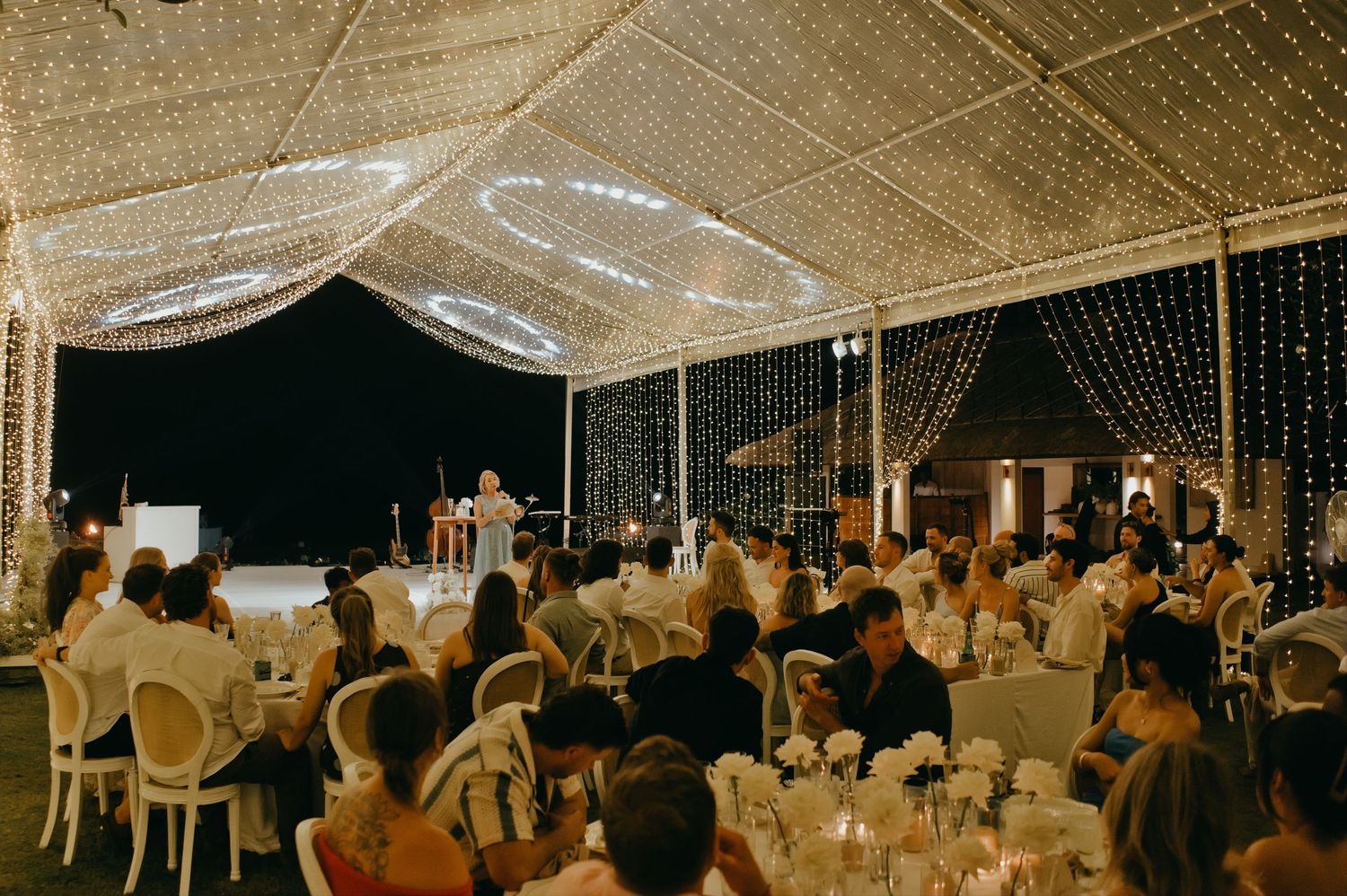Stunning outdoor wedding reception venue with twinkling fairy light canopy and white chairs.
