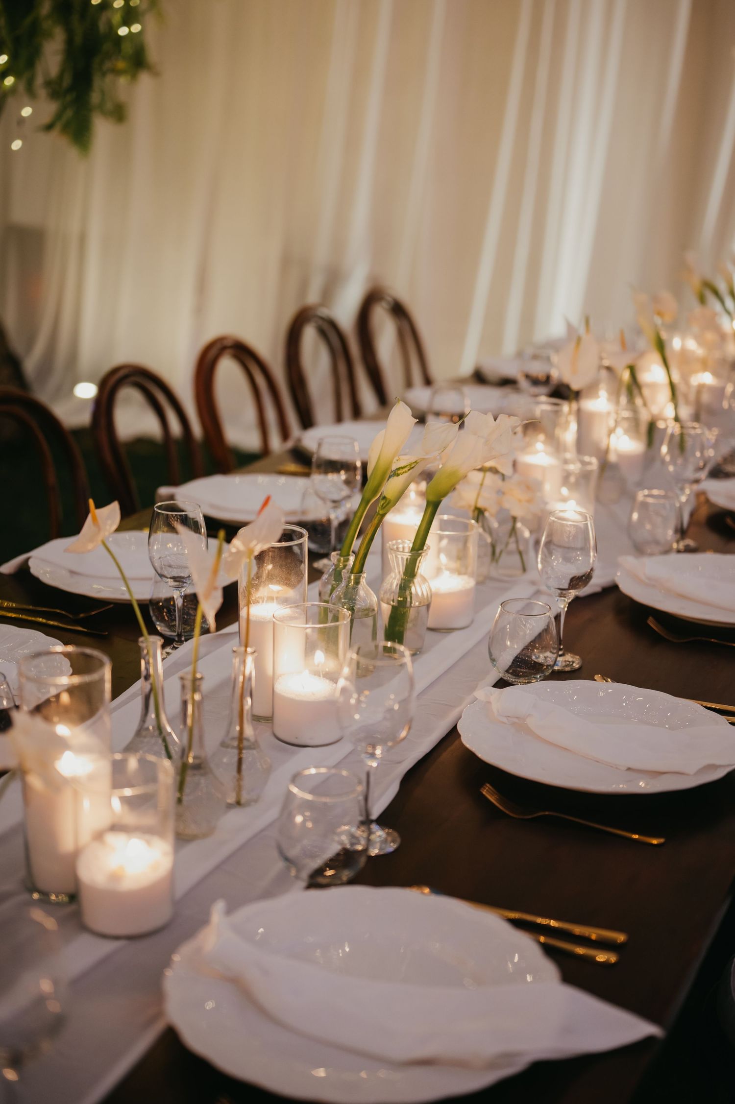 Elegant wedding reception table with white candles, calla lilies, and gold cutlery.