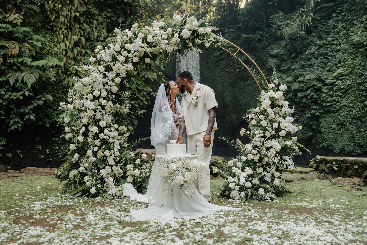 Newlyweds sharing a kiss under a stunning circular white floral arch surrounded by tropical greenery.