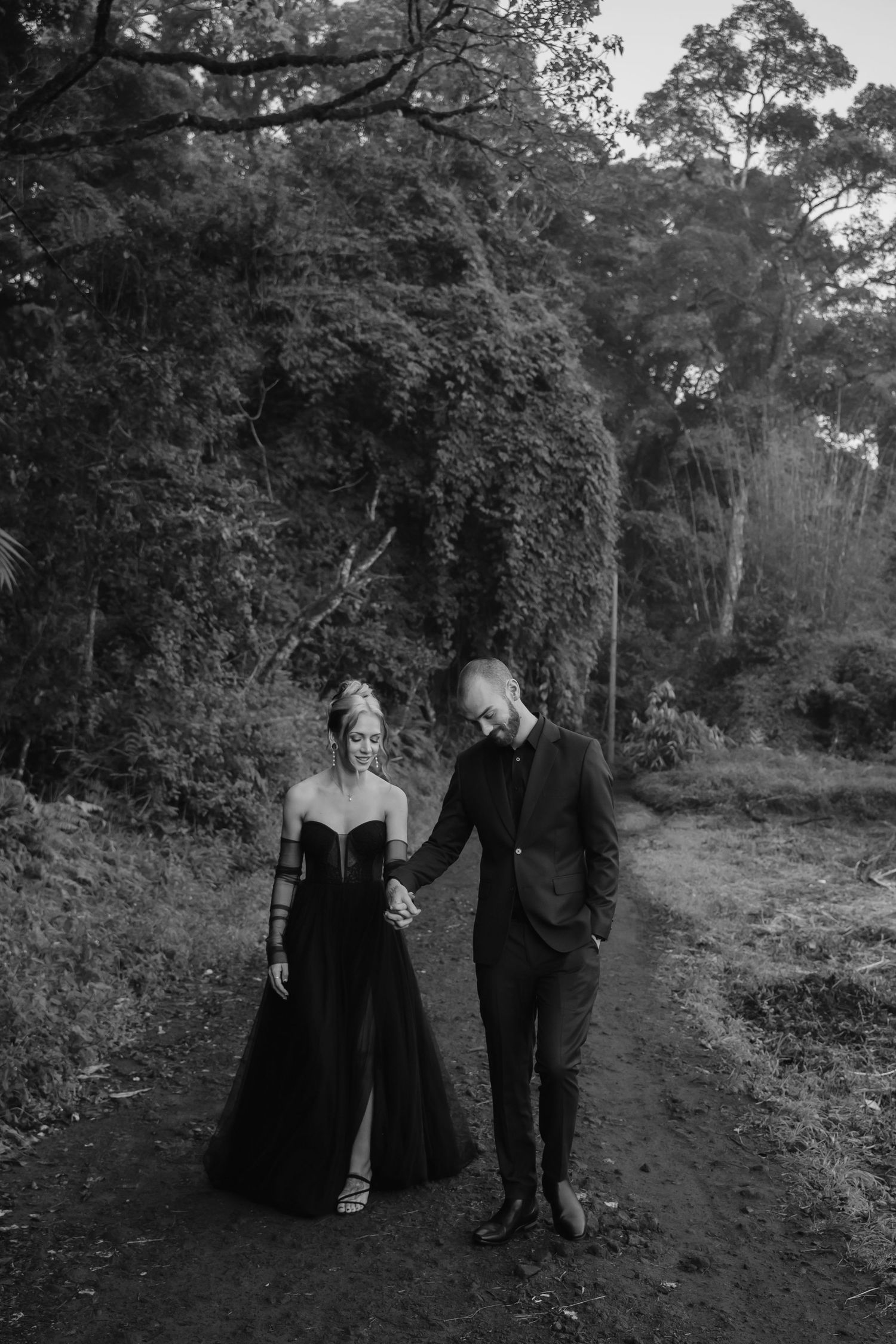 A couple walks together on a wooded forest path in dramatic black and white.