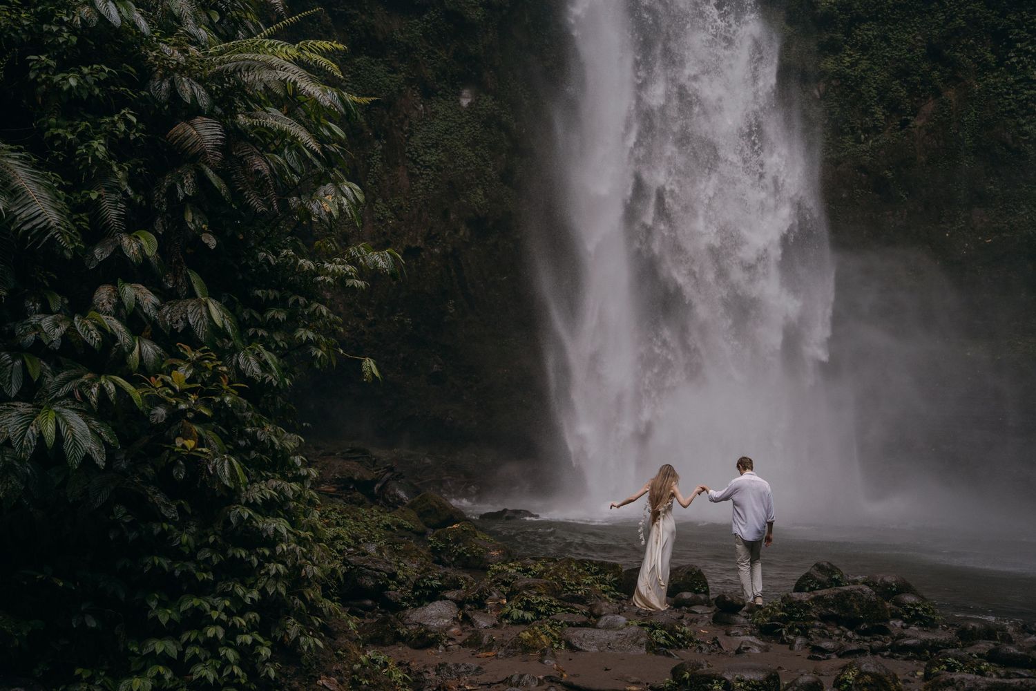 A majestic waterfall cascades down a rocky cliff surrounded by lush tropical vegetation in a rainforest setting.