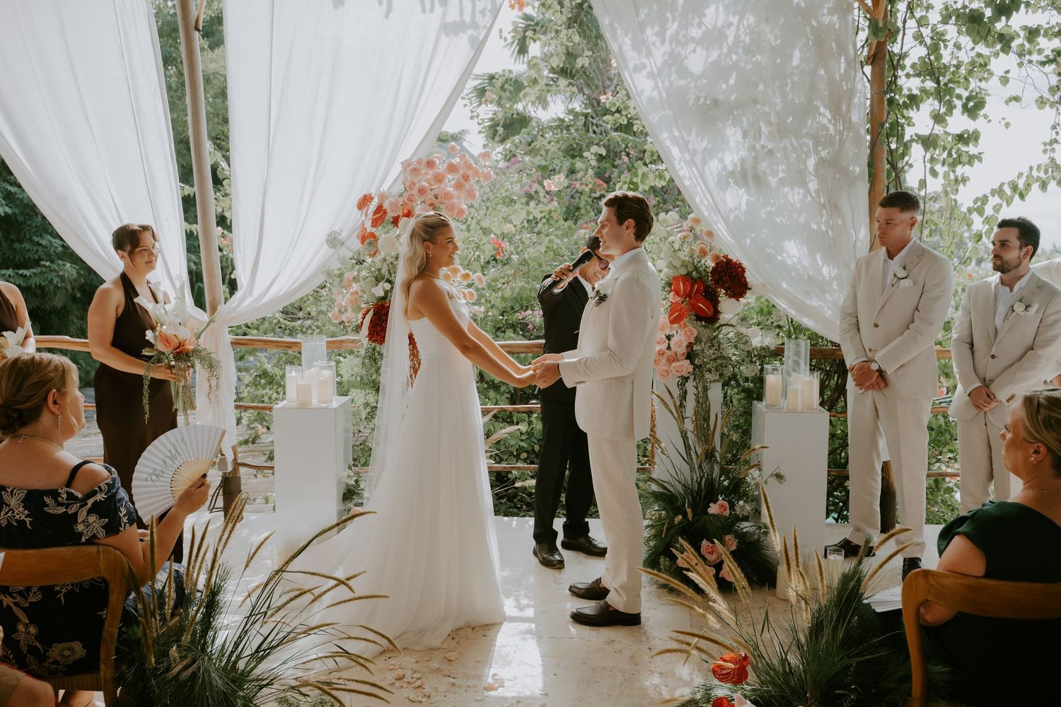 Bride and groom holding hands at a romantic outdoor wedding ceremony surrounded by guests and lush florals.