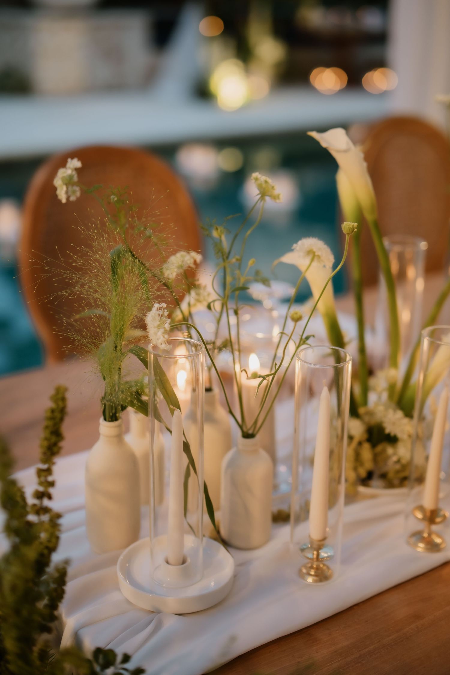 Minimalist wedding table centerpiece featuring white ceramic vases, wildflowers, candles, and champagne flutes.