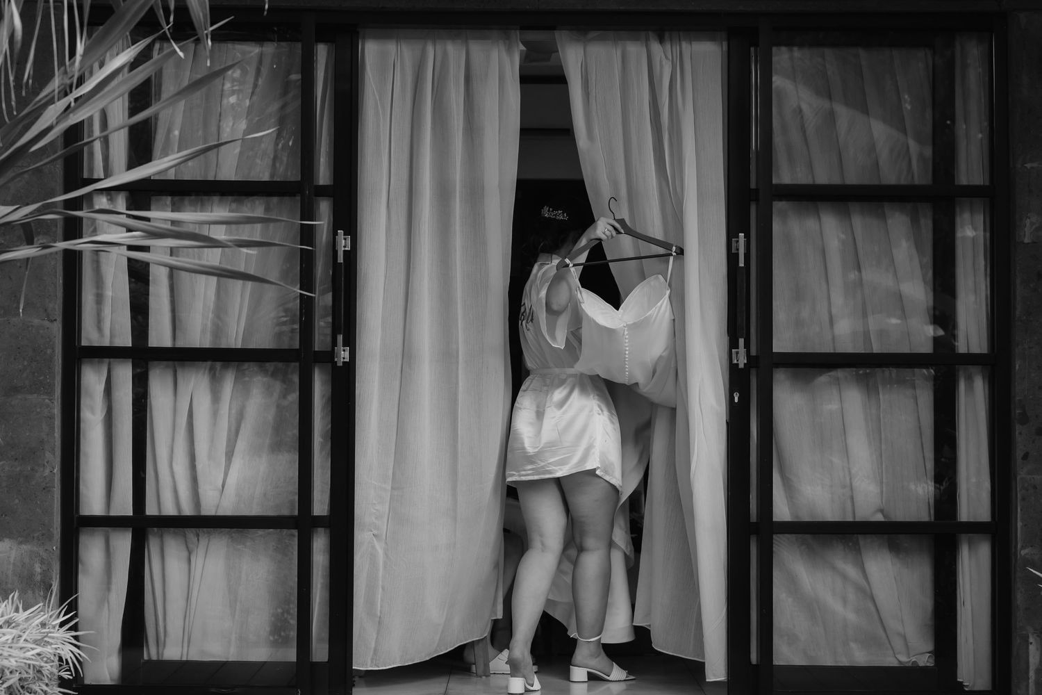 Black and white photo of two people embracing in an open doorway with flowing white curtains.