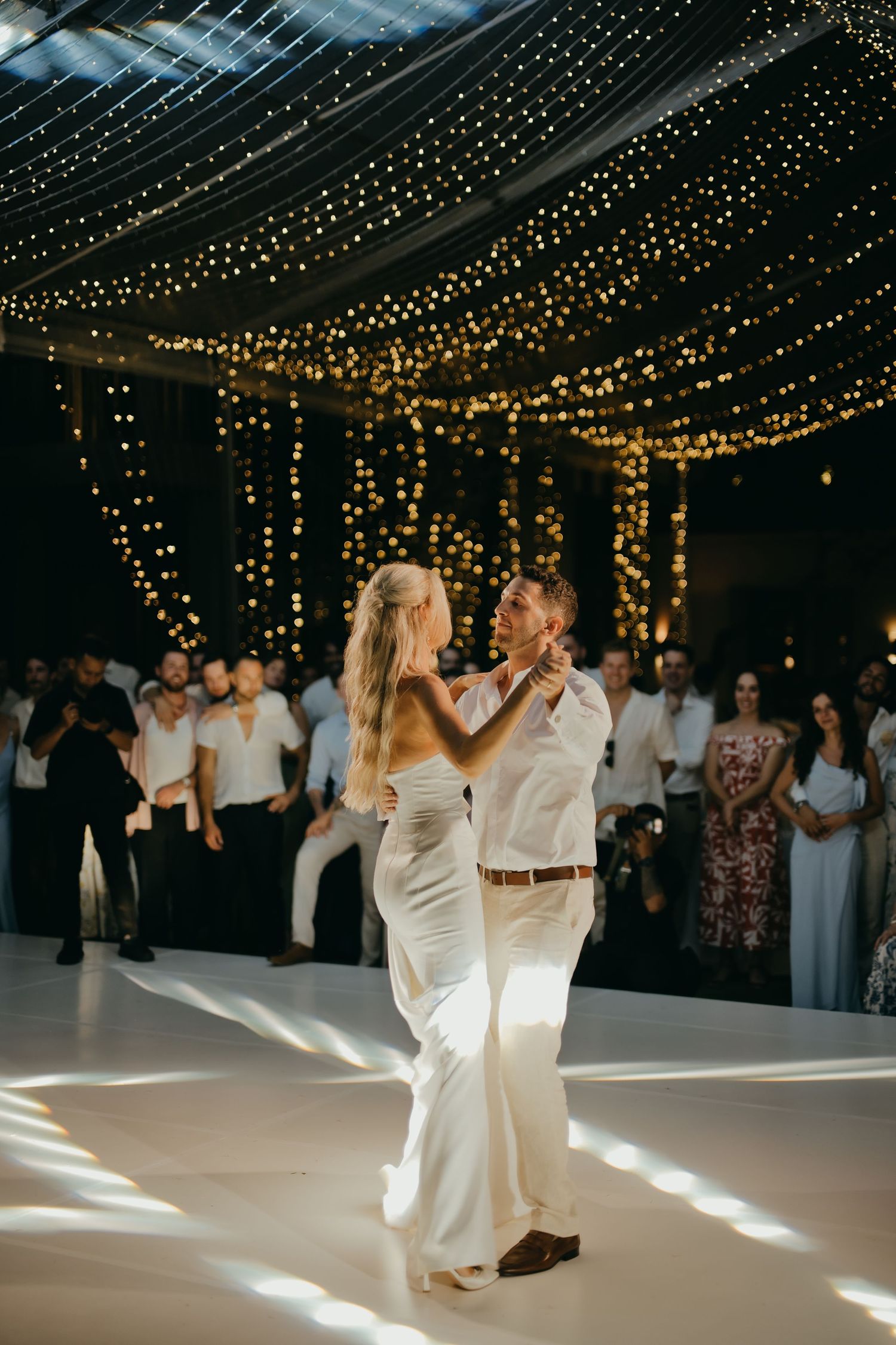 Bride and groom share their first dance under a canopy of glowing fairy lights.