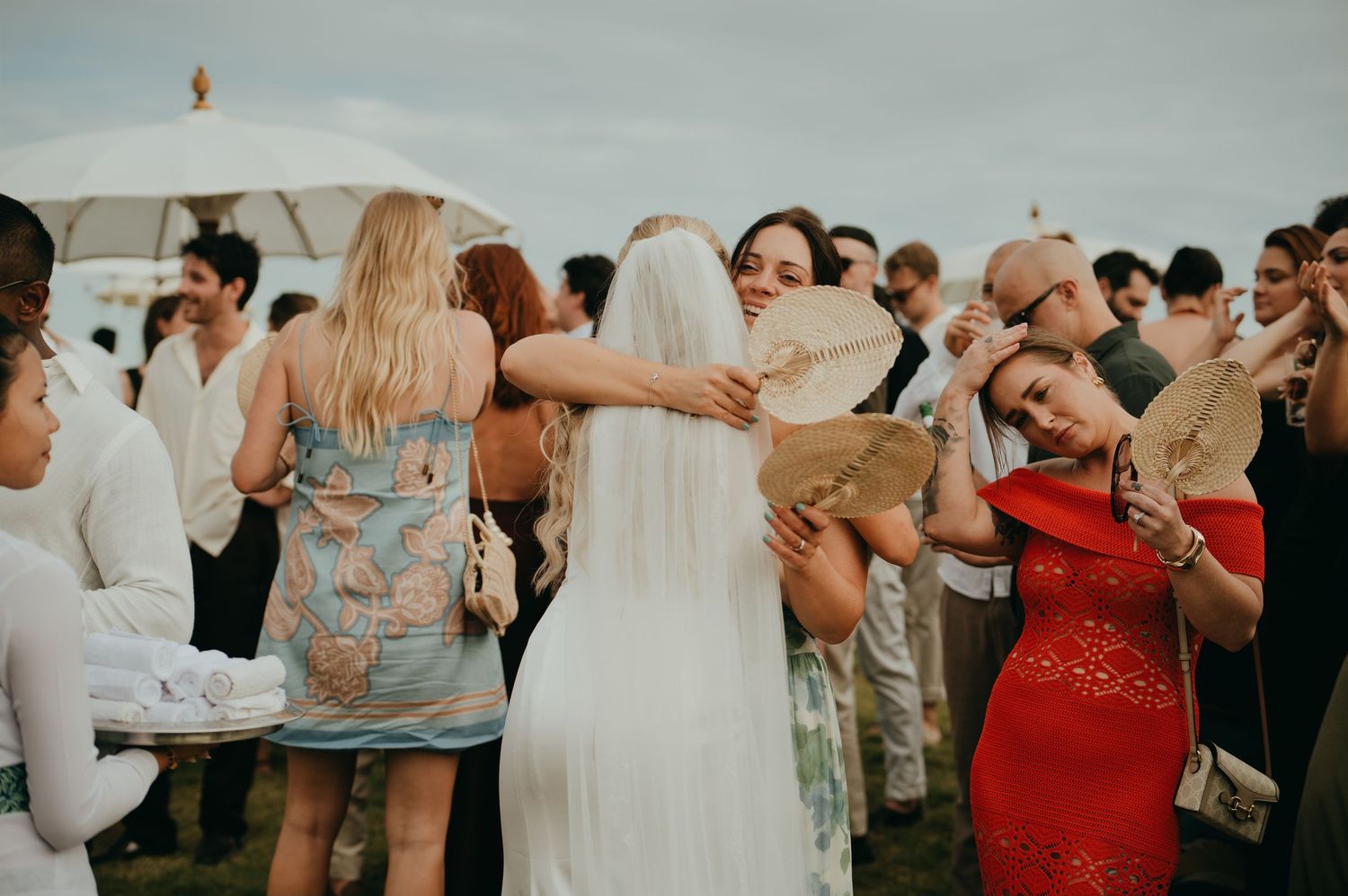 Bride in white gown and veil embraces wedding guests after outdoor ceremony celebration.