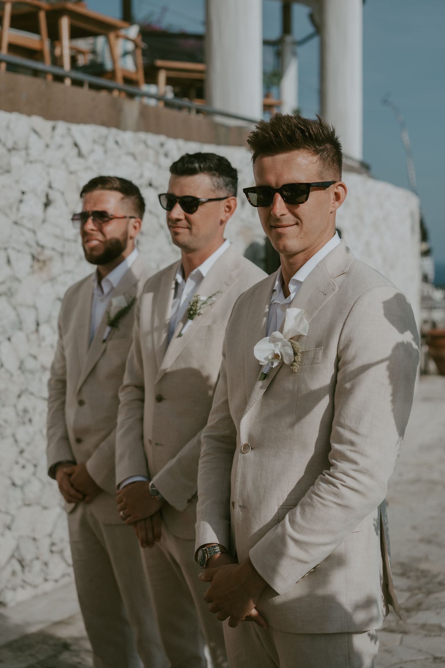 Groomsmen in light beige suits posing together at a destination wedding.