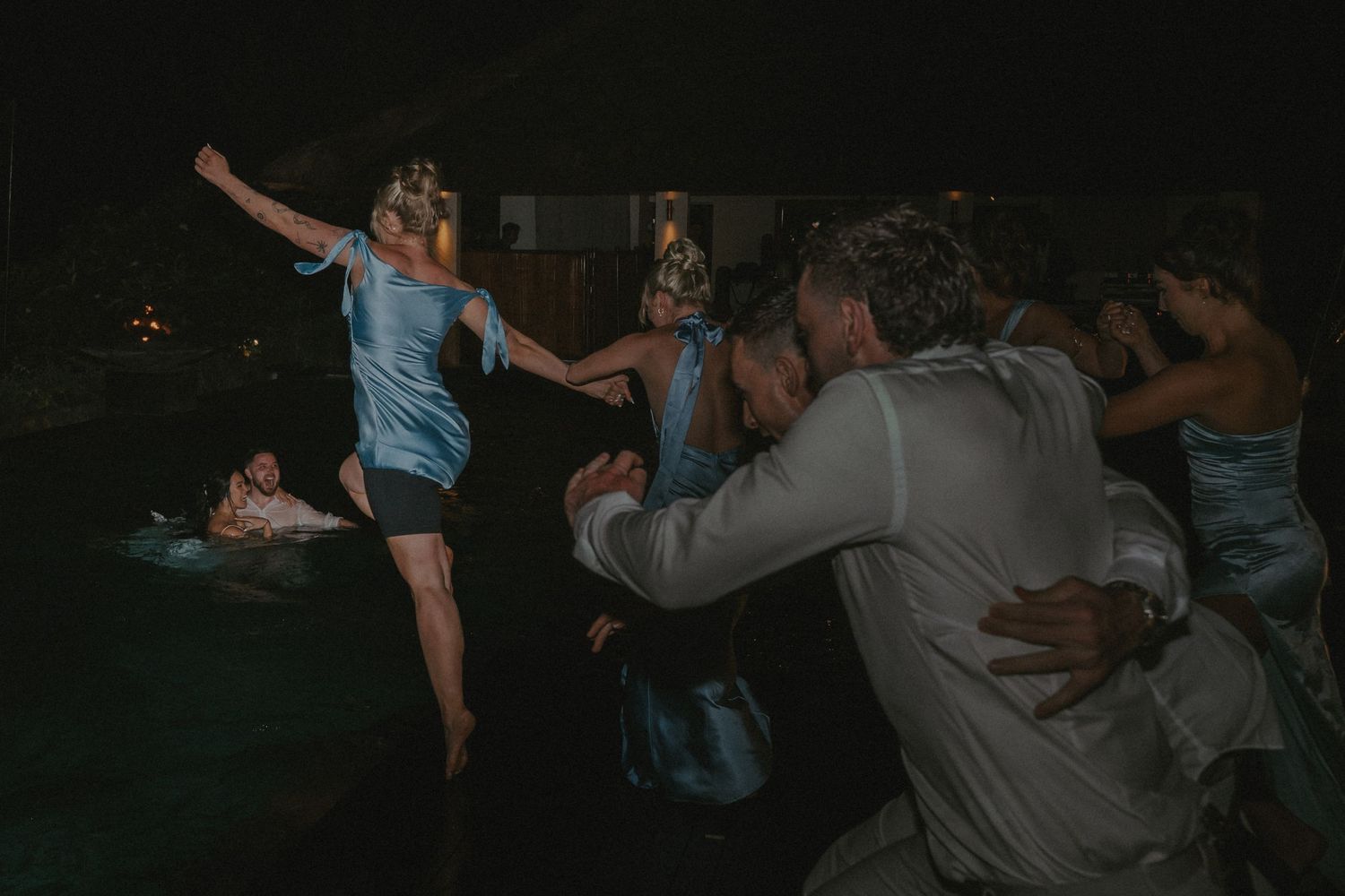 A group of people dancing together at a nighttime outdoor event with string lights overhead.