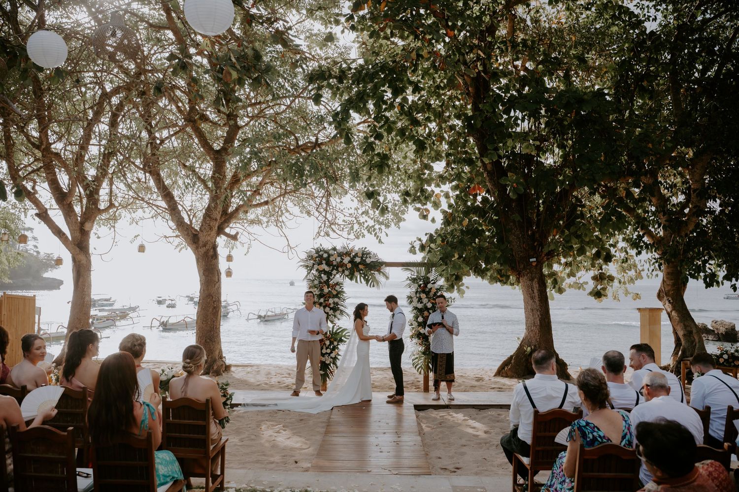 A couple shares their first dance at an intimate outdoor wedding ceremony under trees at dusk.