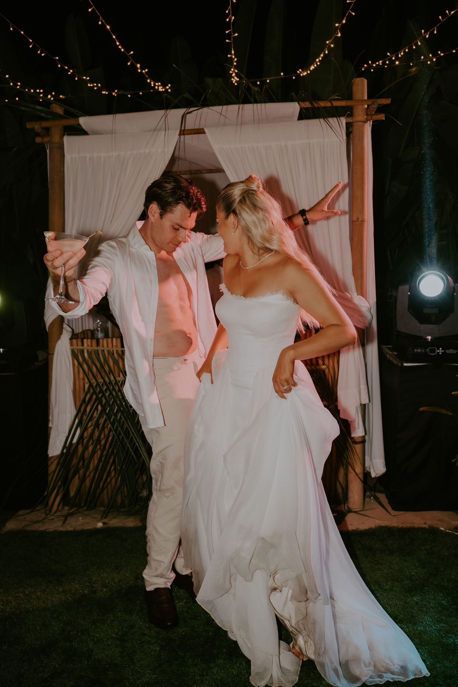 Bride and groom dance together under string lights at outdoor tropical wedding reception.