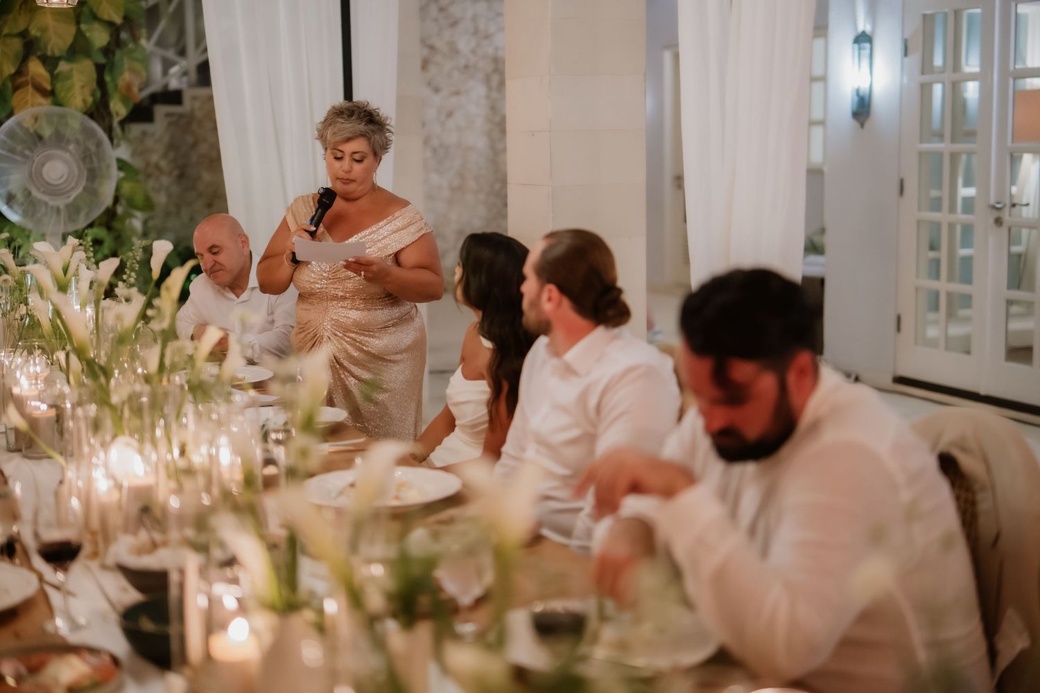 Elegant wedding reception dinner with guest giving a heartfelt speech at a candlelit table.