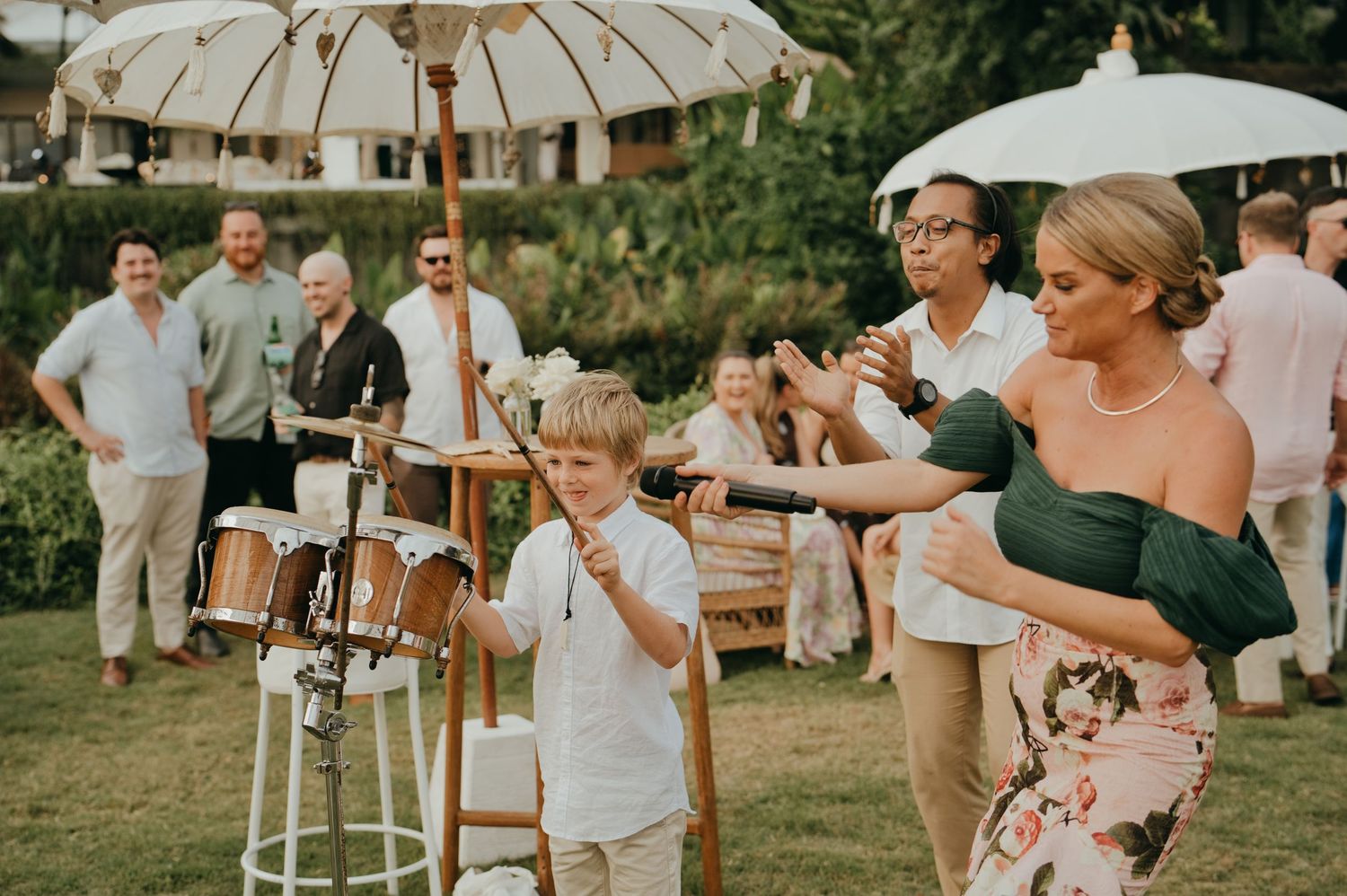Young boy plays drums at a wedding reception while guests enjoy the outdoor entertainment.