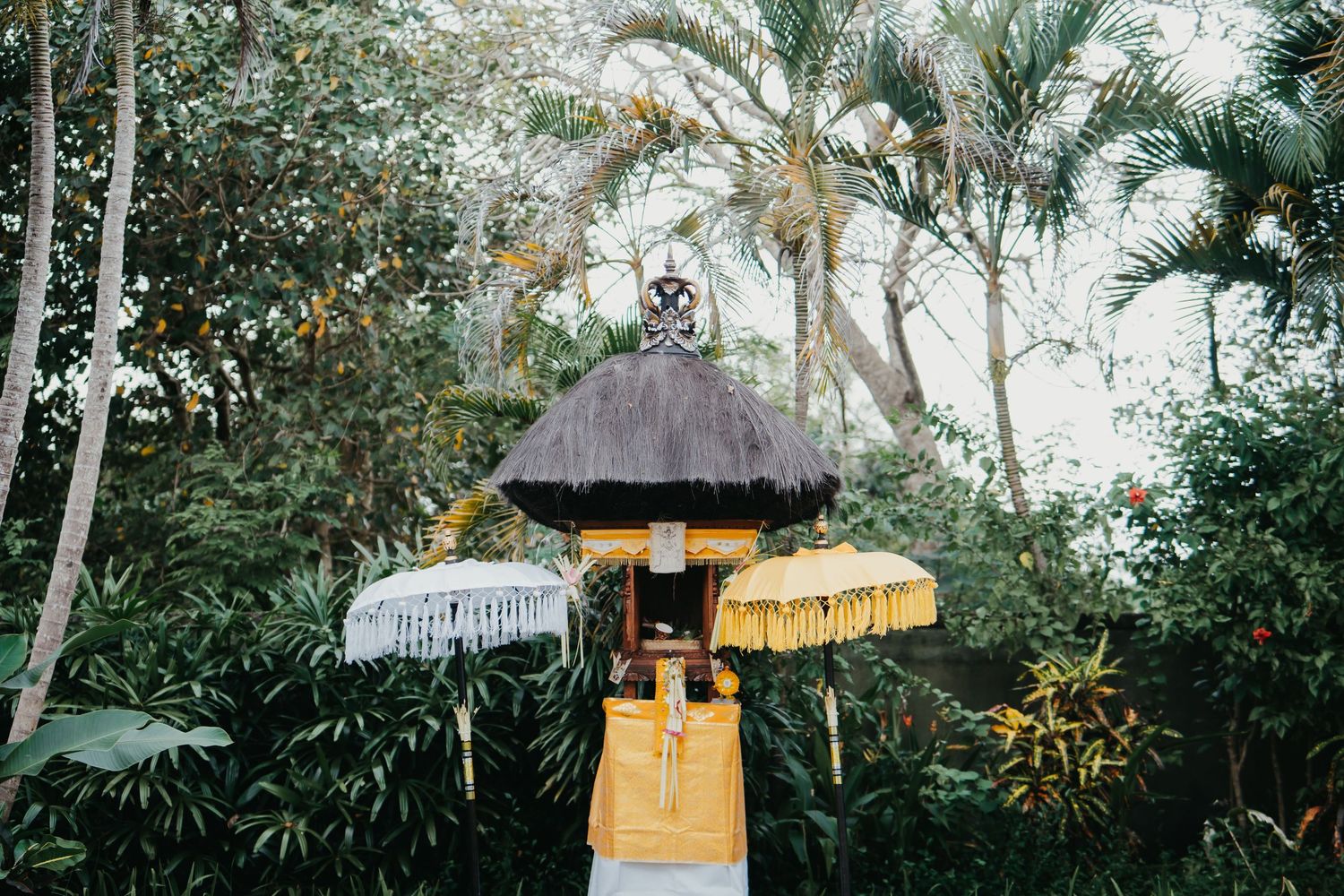 Traditional Balinese shrine decorated with yellow and white offerings in tropical garden.