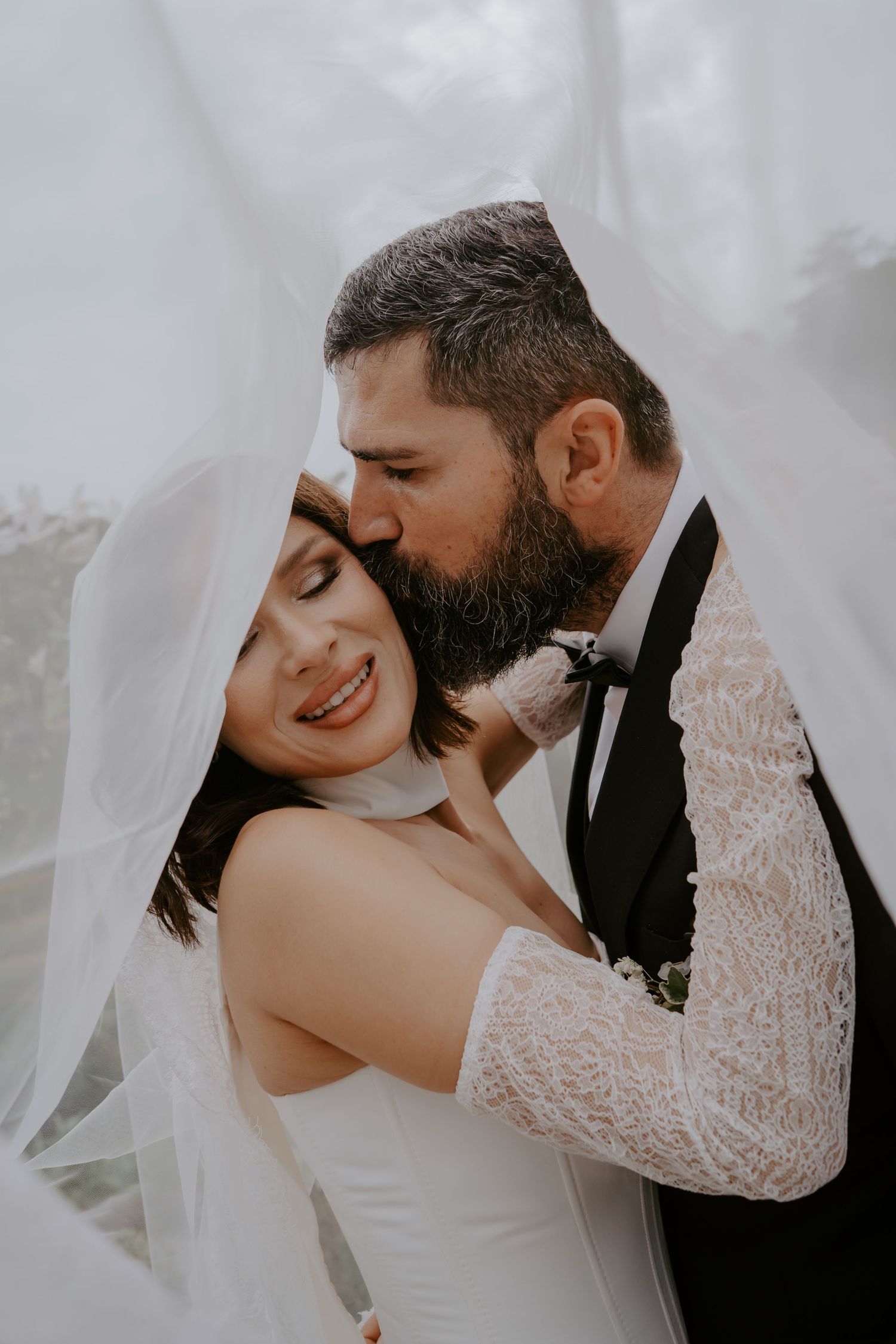 A romantic wedding couple embraces under flowing white curtains in an intimate portrait series.