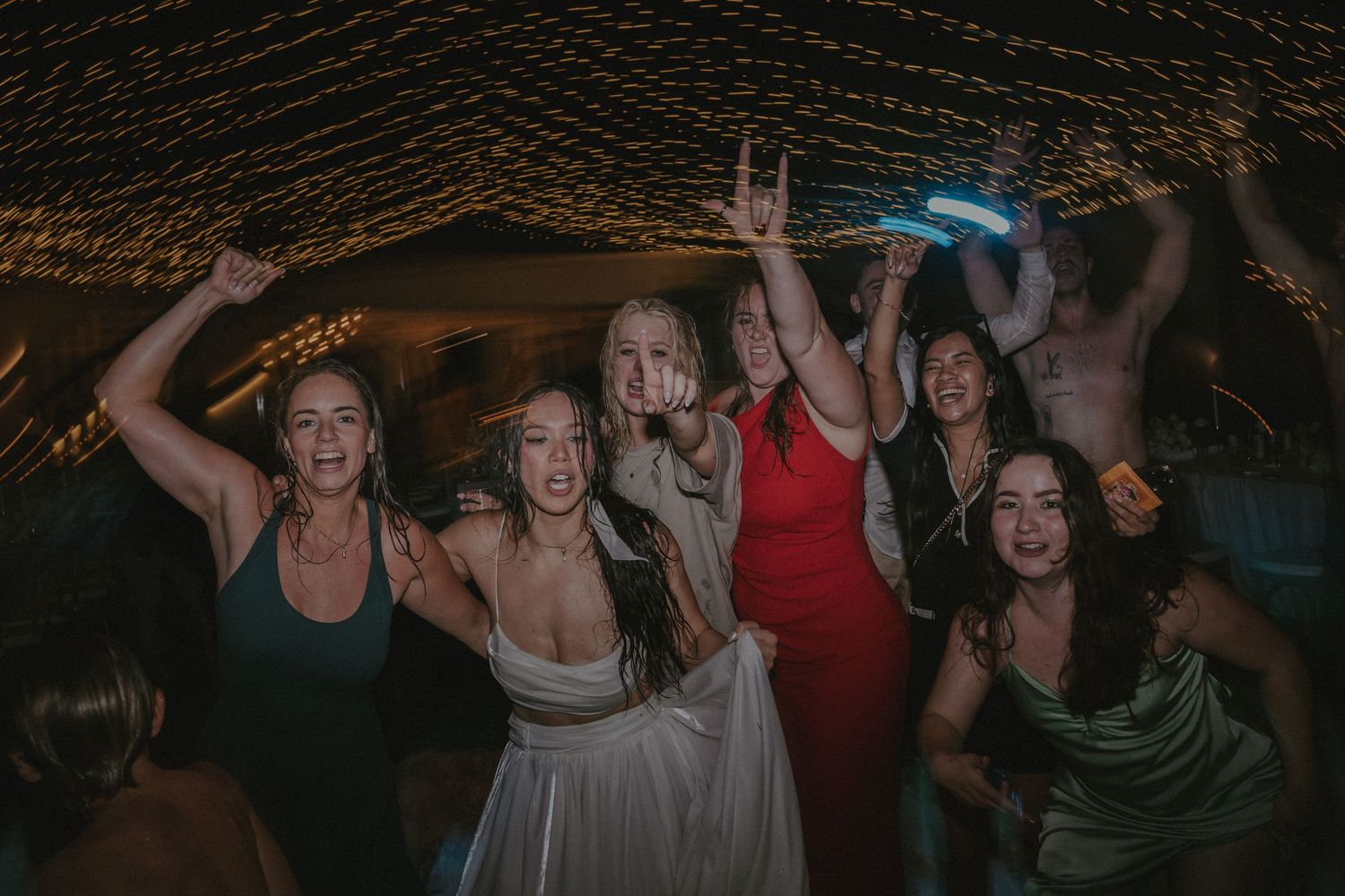 A lively crowd dances and celebrates together on a dimly lit dance floor at a nighttime event.