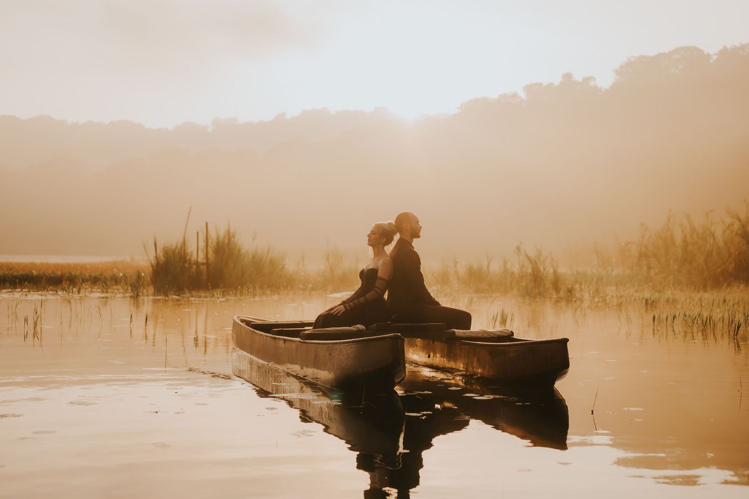 Two people in silhouette sit in a small boat on a tranquil lake during golden hour.