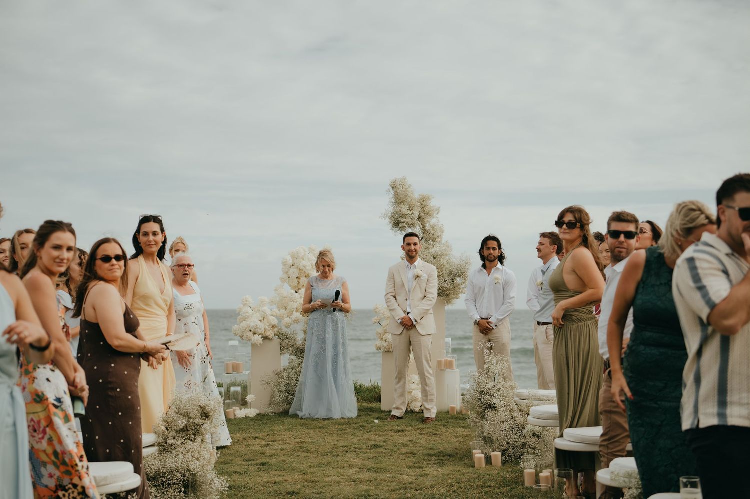 Outdoor beach wedding ceremony with guests gathered as couple exchanges vows by the ocean.