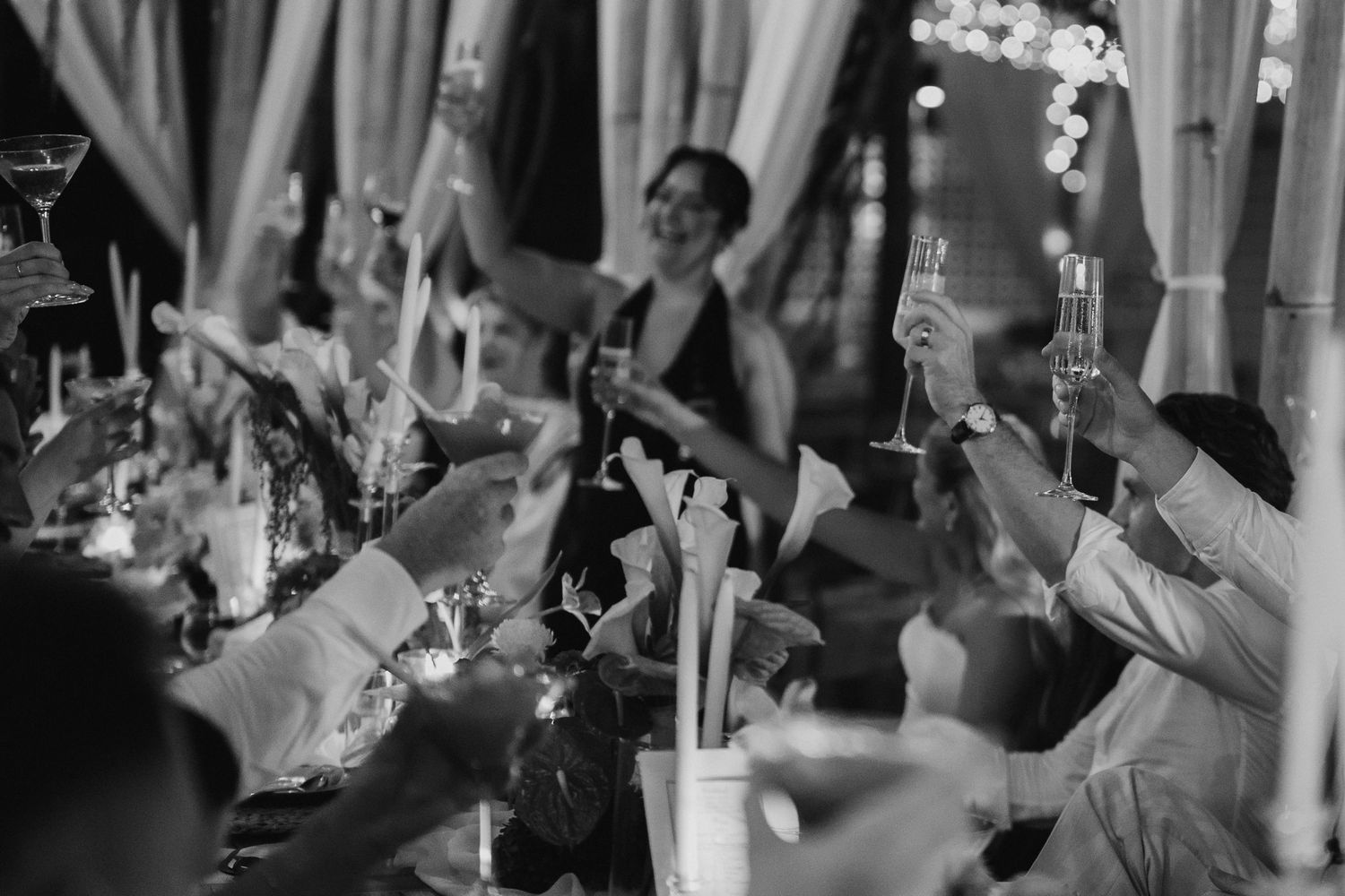 Black and white photo of wedding guests raising glasses in a champagne toast.