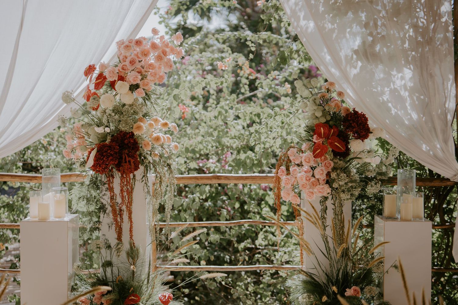 Romantic wedding ceremony arch adorned with lush pink and burgundy floral arrangements and white draping outdoors.