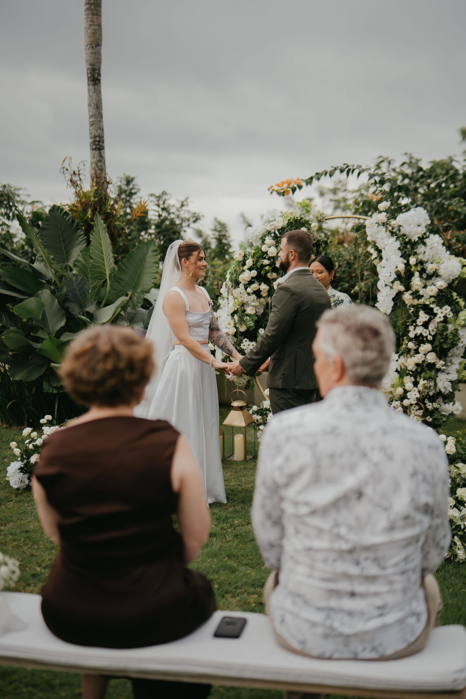Bride and groom exchange vows at outdoor garden wedding ceremony with small group of guests.